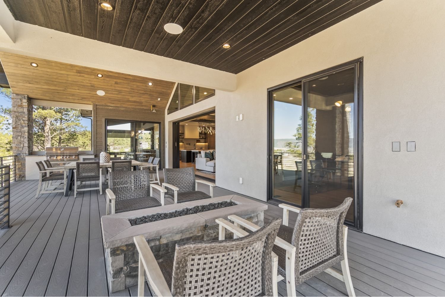Outdoor Trex deck area with seating, a fire pit, and a view of trees through open sliding glass doors.