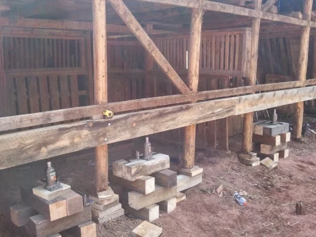 Construction site with wooden framework and cribbing supporting horizontal wooden beams used to raise the barn to install concrete to support the rotted posts.