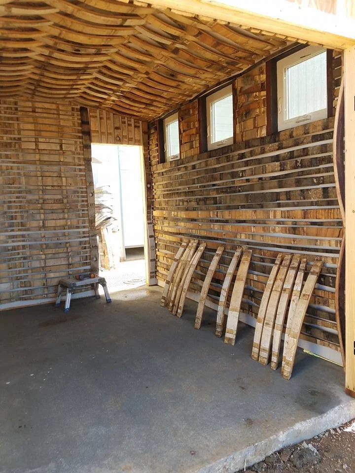 Interior of a wooden structure with slatted walls and ceiling, four small windows, and several wooden sleds leaning against the wall.