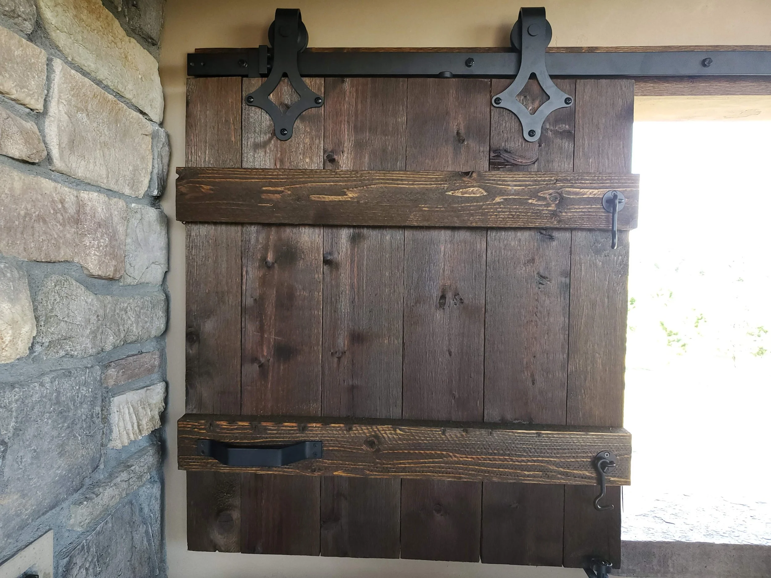 A rustic wooden door with black metal hardware, including handles, hinges, and a latch, set in a stone wall with large, irregularly shaped stones.