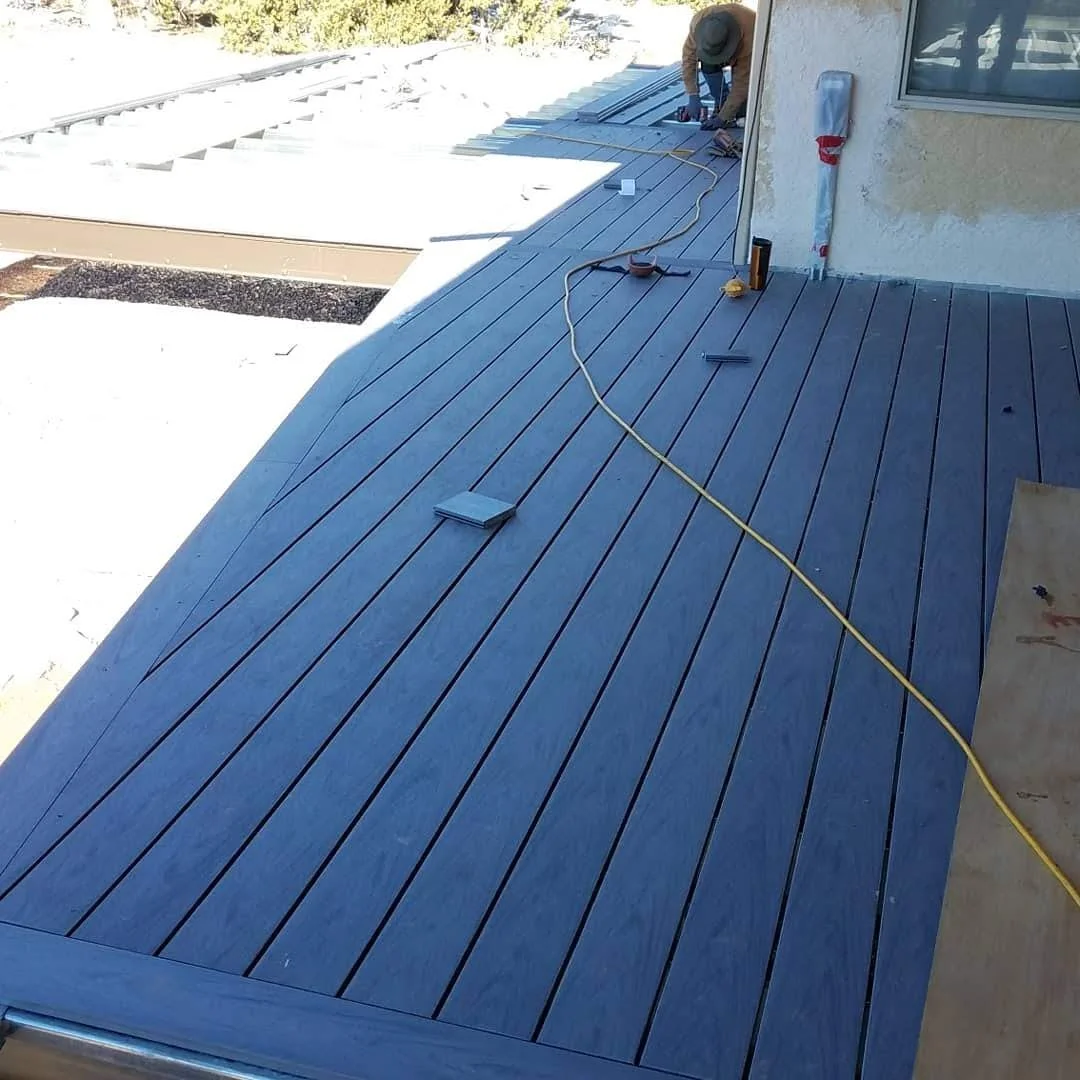 A construction worker installing a Tres deck on a patio, with tools and materials around him.