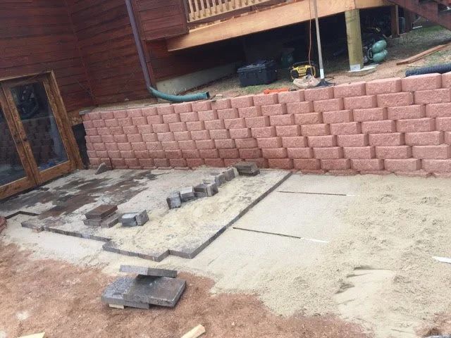 In-progress construction site with a new stone wall and a concrete patio made of pavers area.