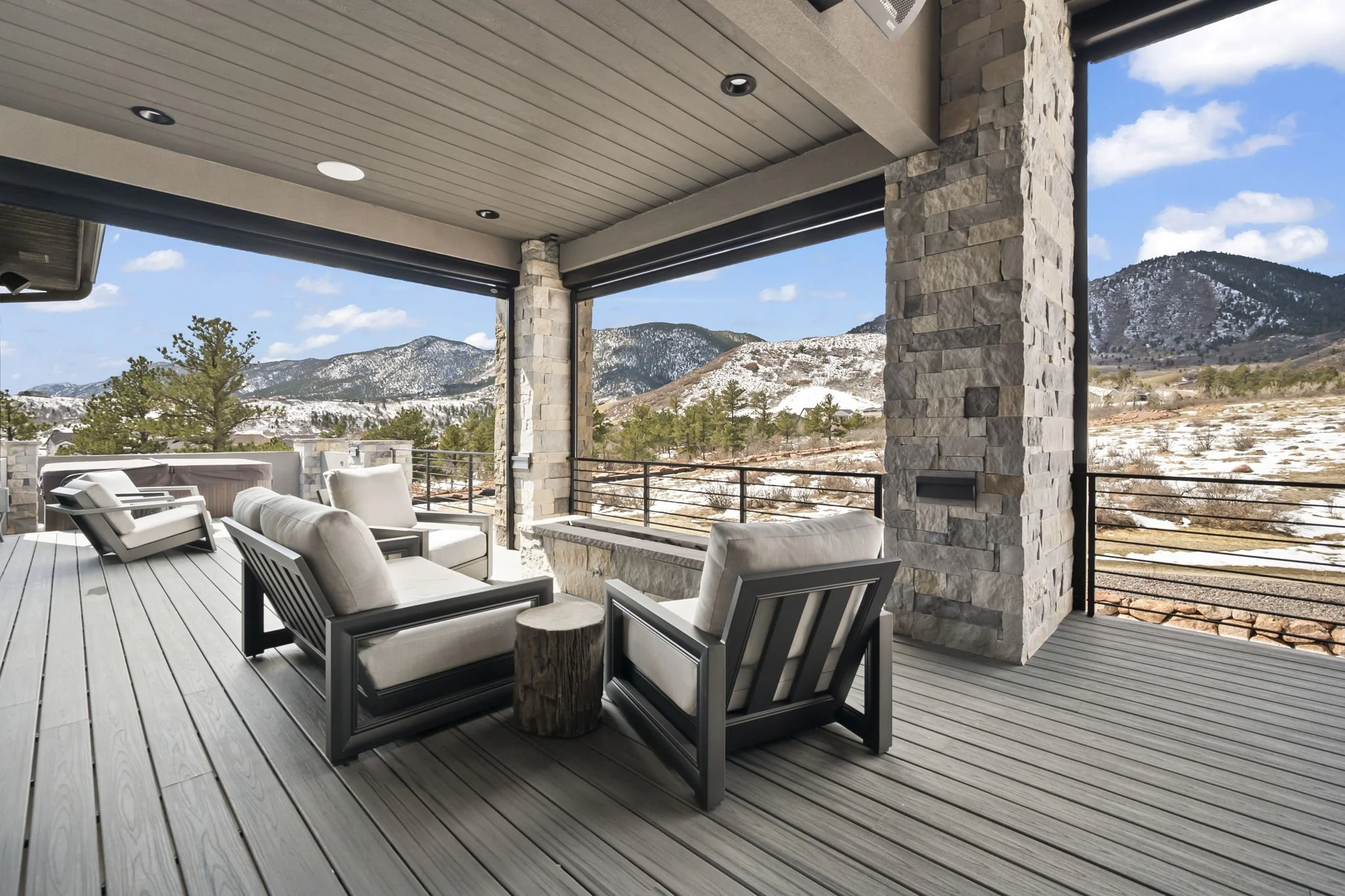 Outdoor deck with white cushioned chairs and a small wooden side table, surrounded by stone columns and a scenic mountain view in the background.