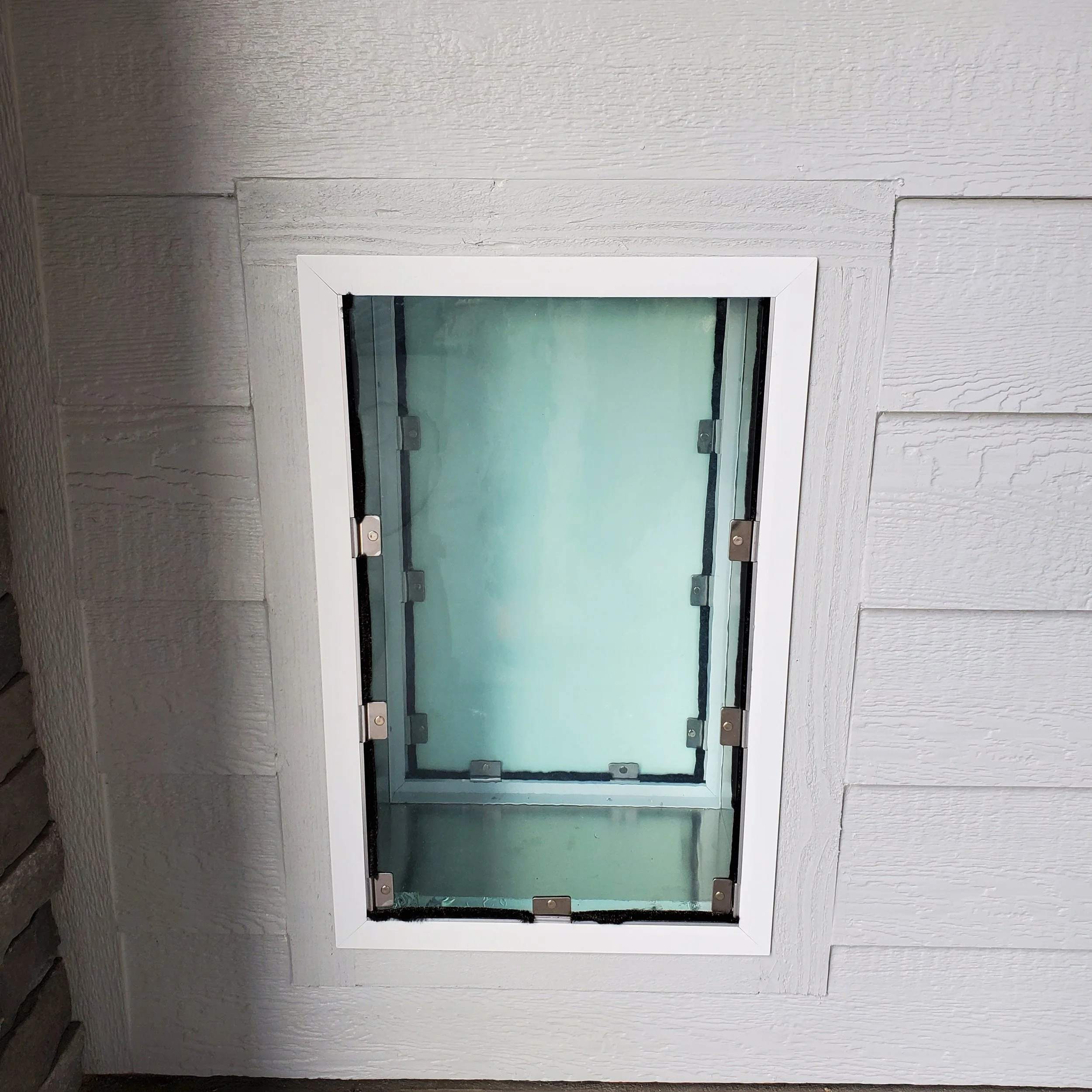 A dog door on the exterior wall beneath a white-washed wood siding.