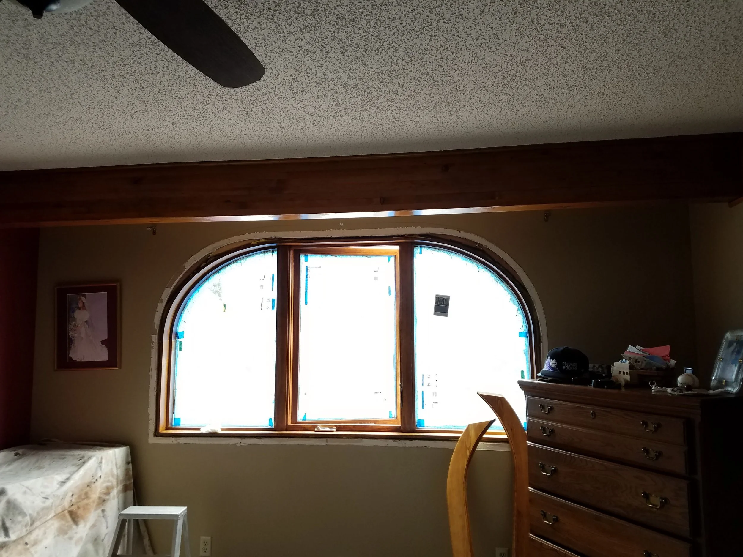 Installation of a  large arched window,  custom wood trim wooden furniture, table with marble top, and various items on furniture.