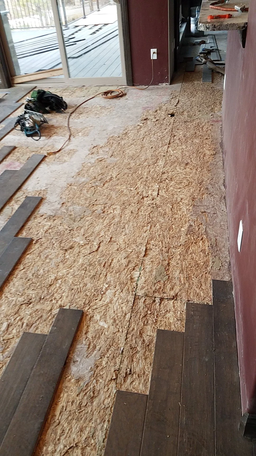 Interior of a home undergoing renovation, with a partially removed floor revealing insulation and subfloor, with tools and construction materials scattered around.