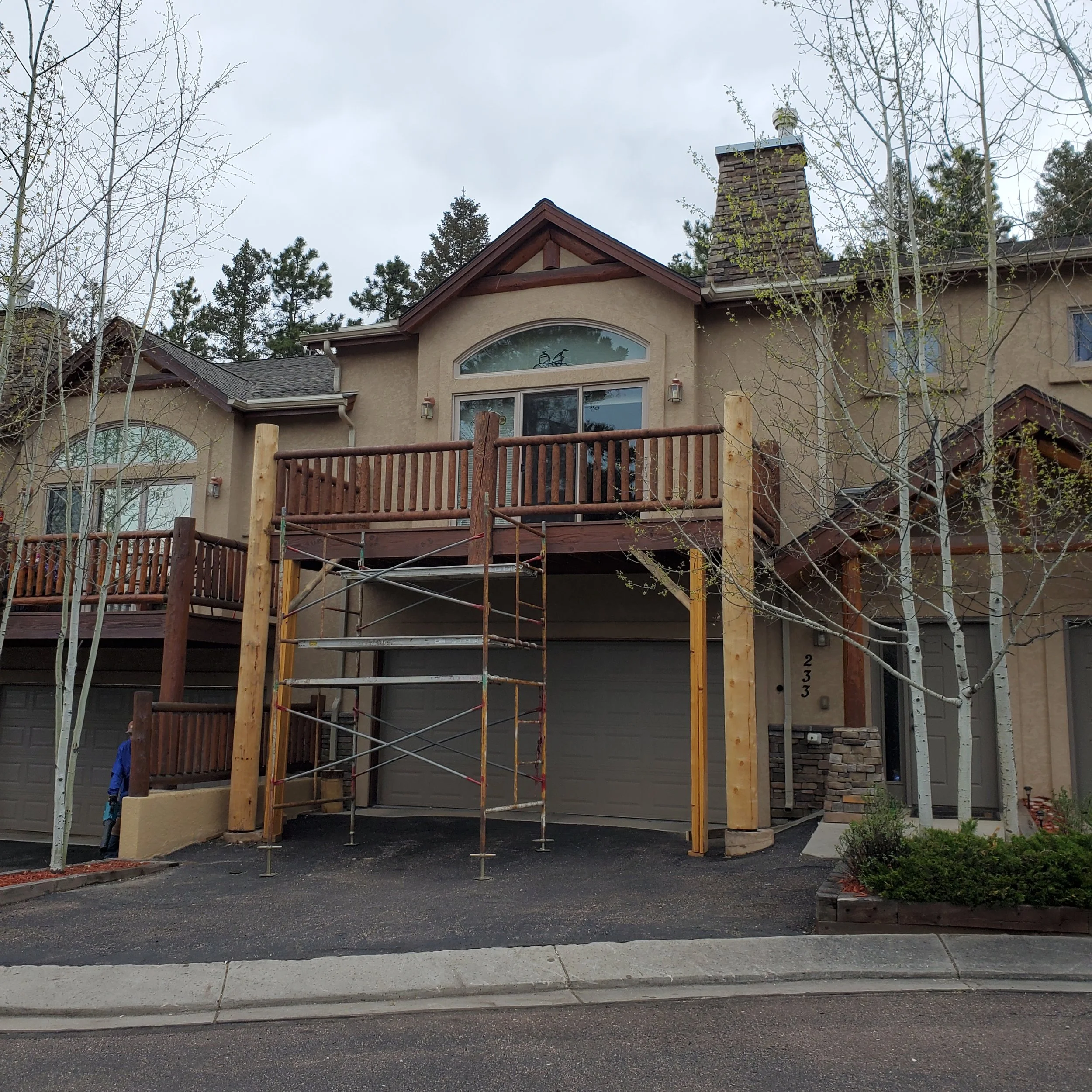 House under construction with scaffolding in front, surrounded by trees with no leaves and an overcast sky.
