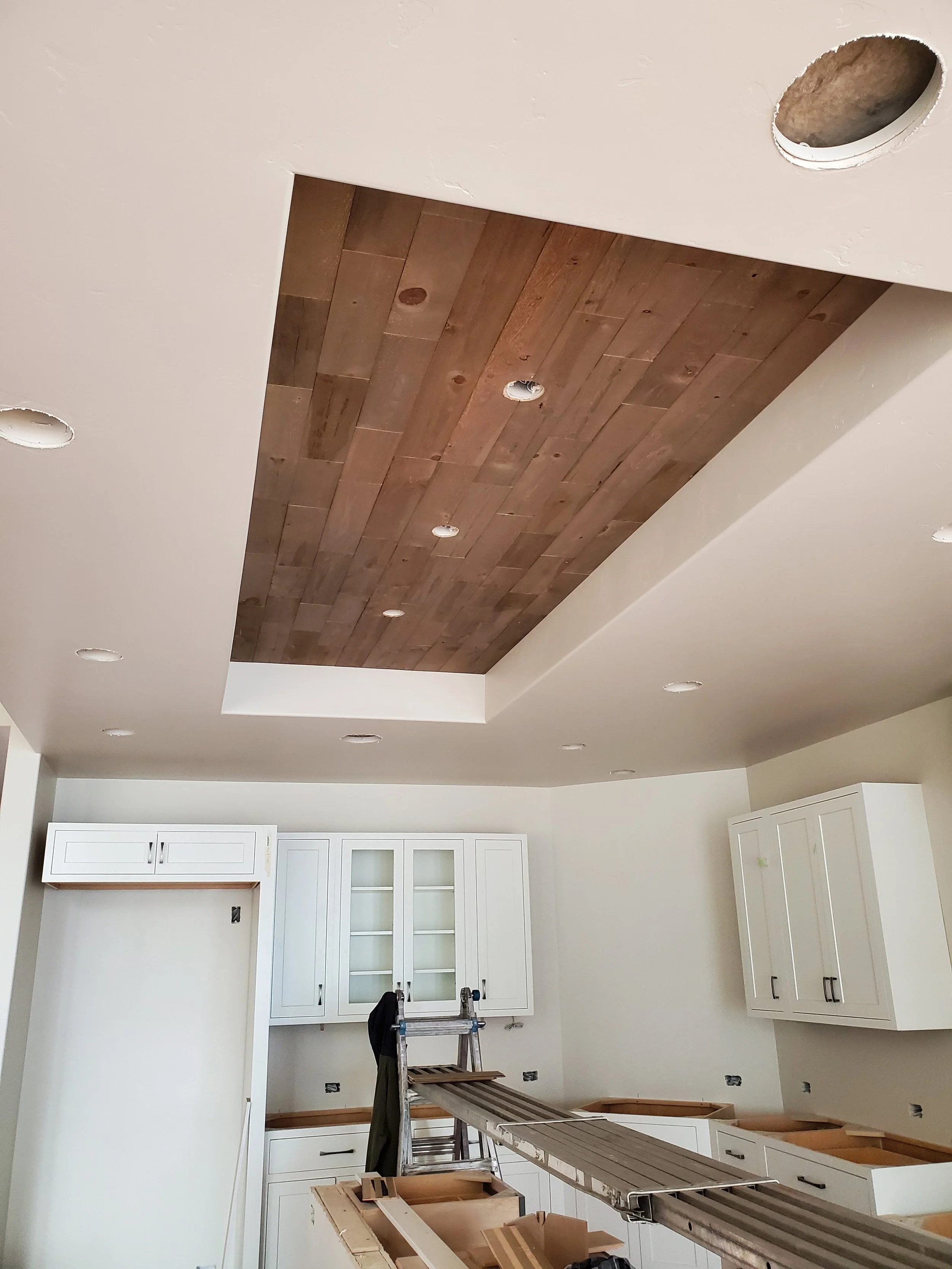 Interior room with a wooden ceiling, white cabinets, a ladder, and construction tools, indicating ongoing renovation or construction work.