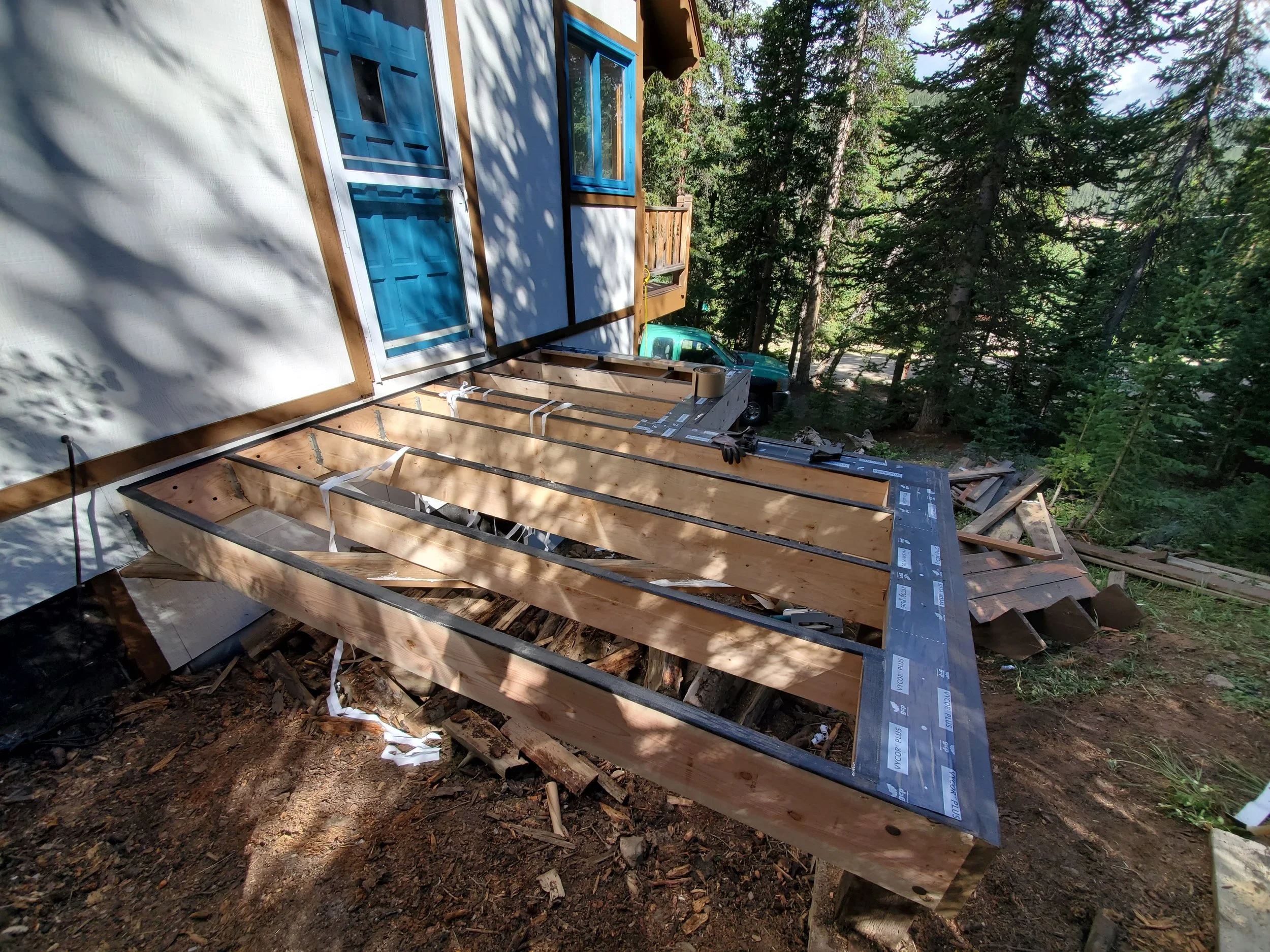 Under construction of a house showing framework and blue sliding door with a forested area in the background.
