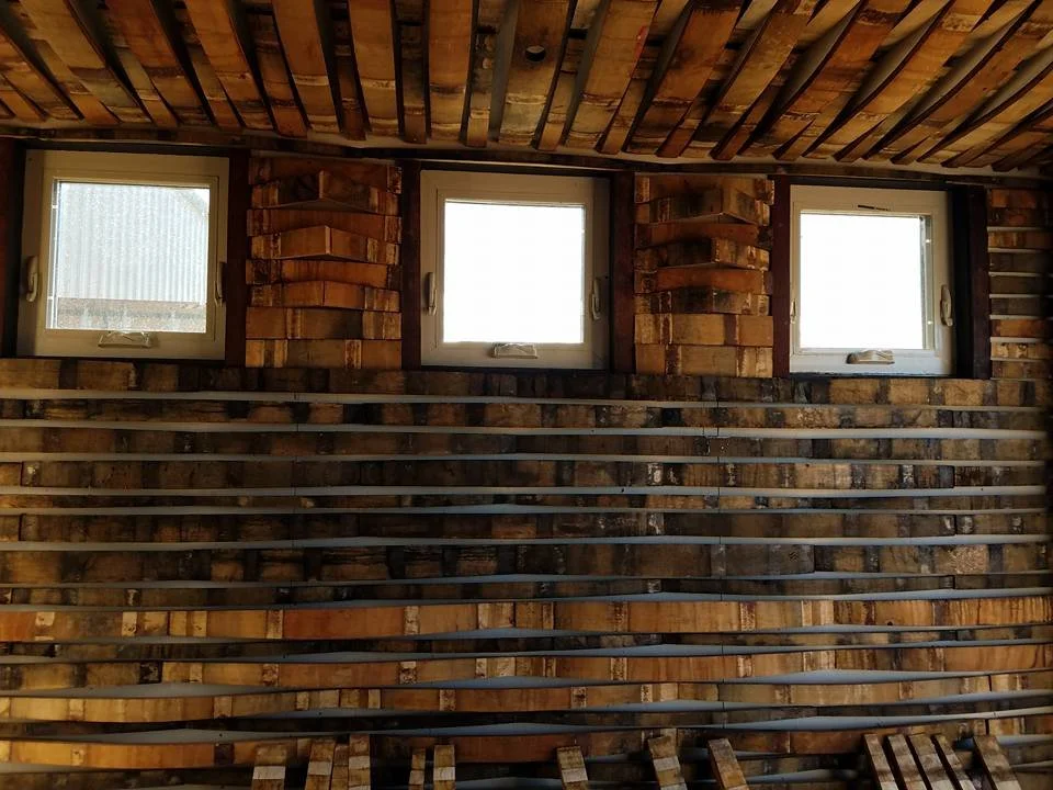 Three small windows in a brick wall with exposed wiring and wood beams on the ceiling.