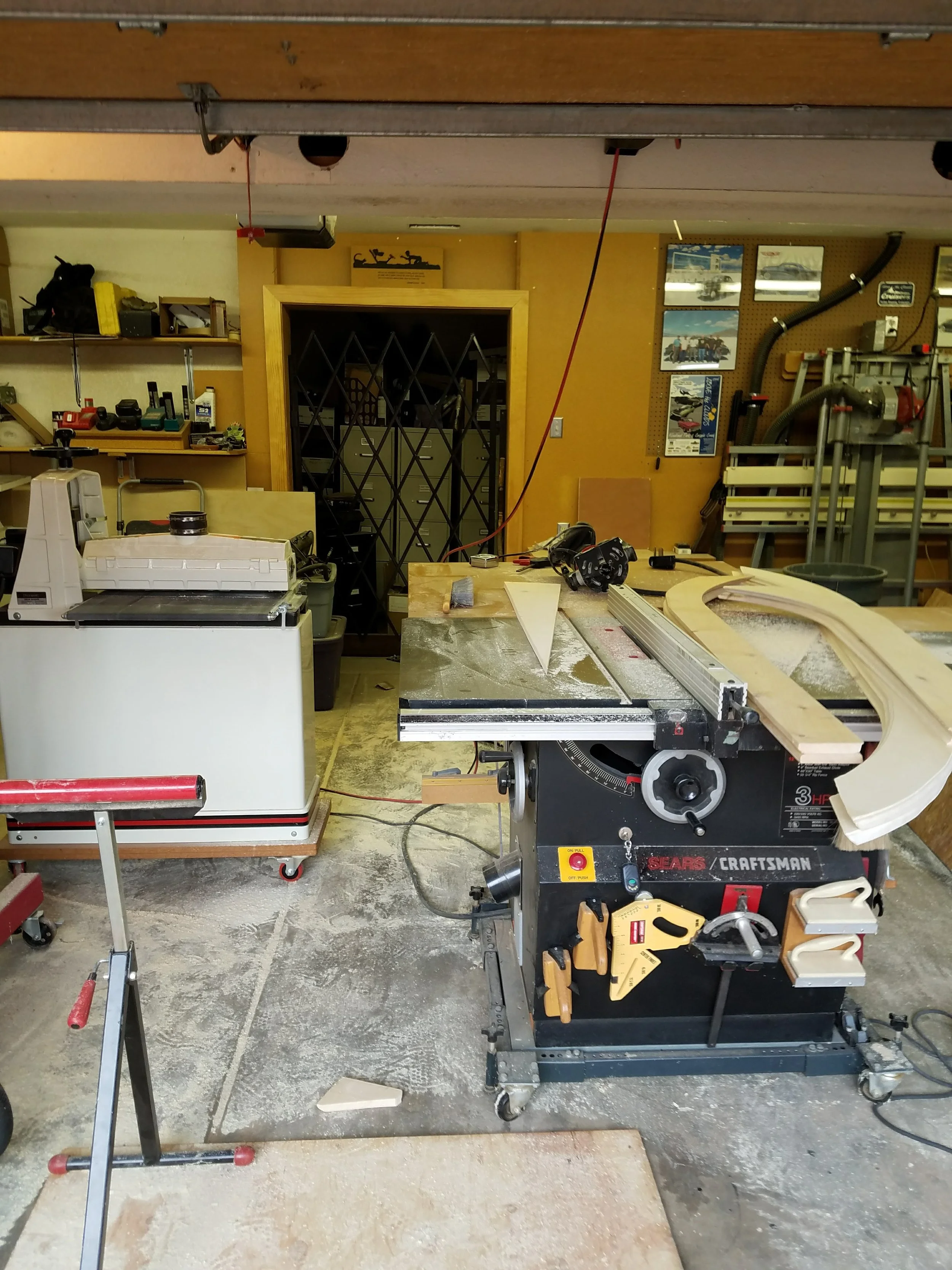 A woodworking workshop with a Craftsman table saw, a workbench, and various tools and equipment on shelves and the wall.