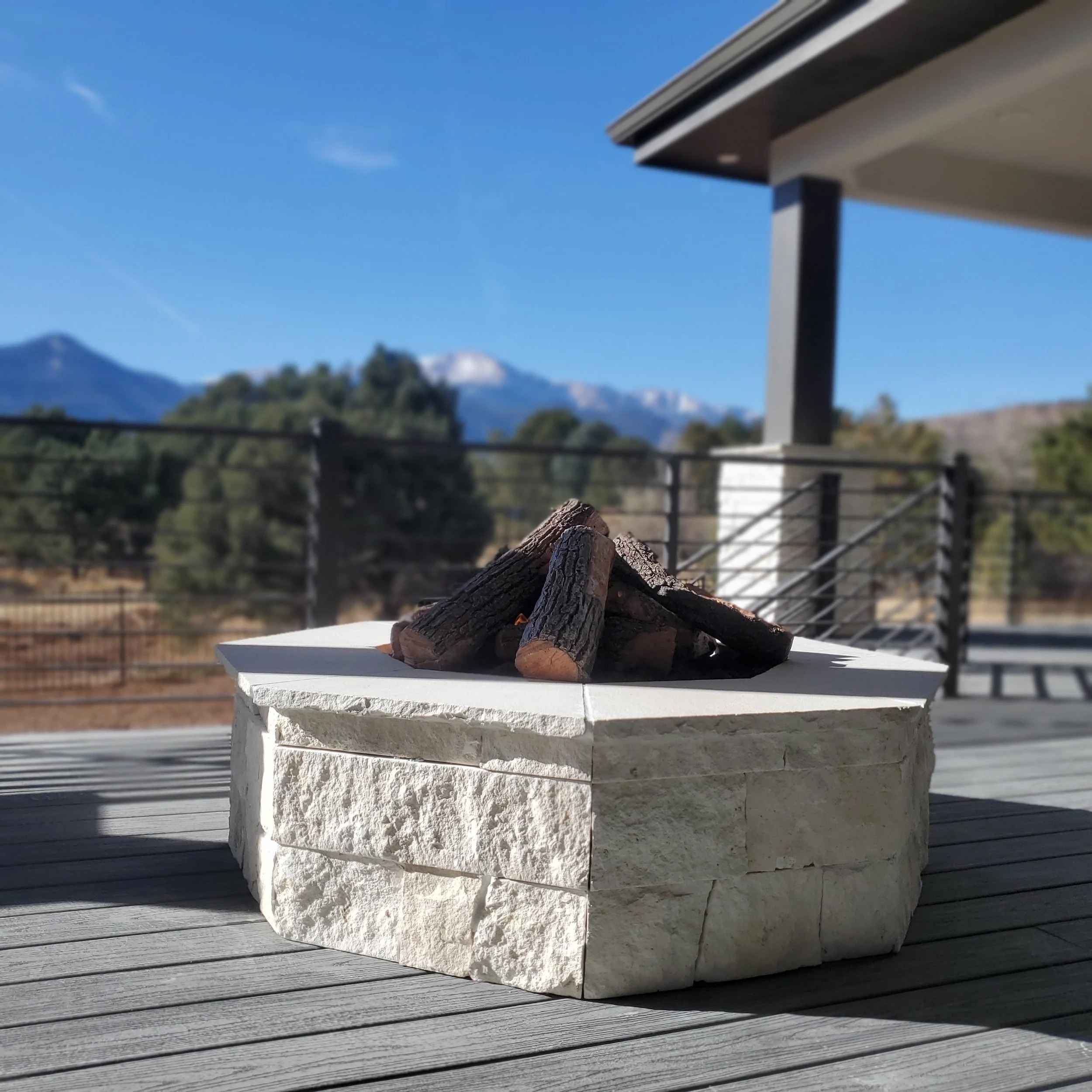 Pile of firewood on a white stone platform outdoors with mountain and blue sky background.