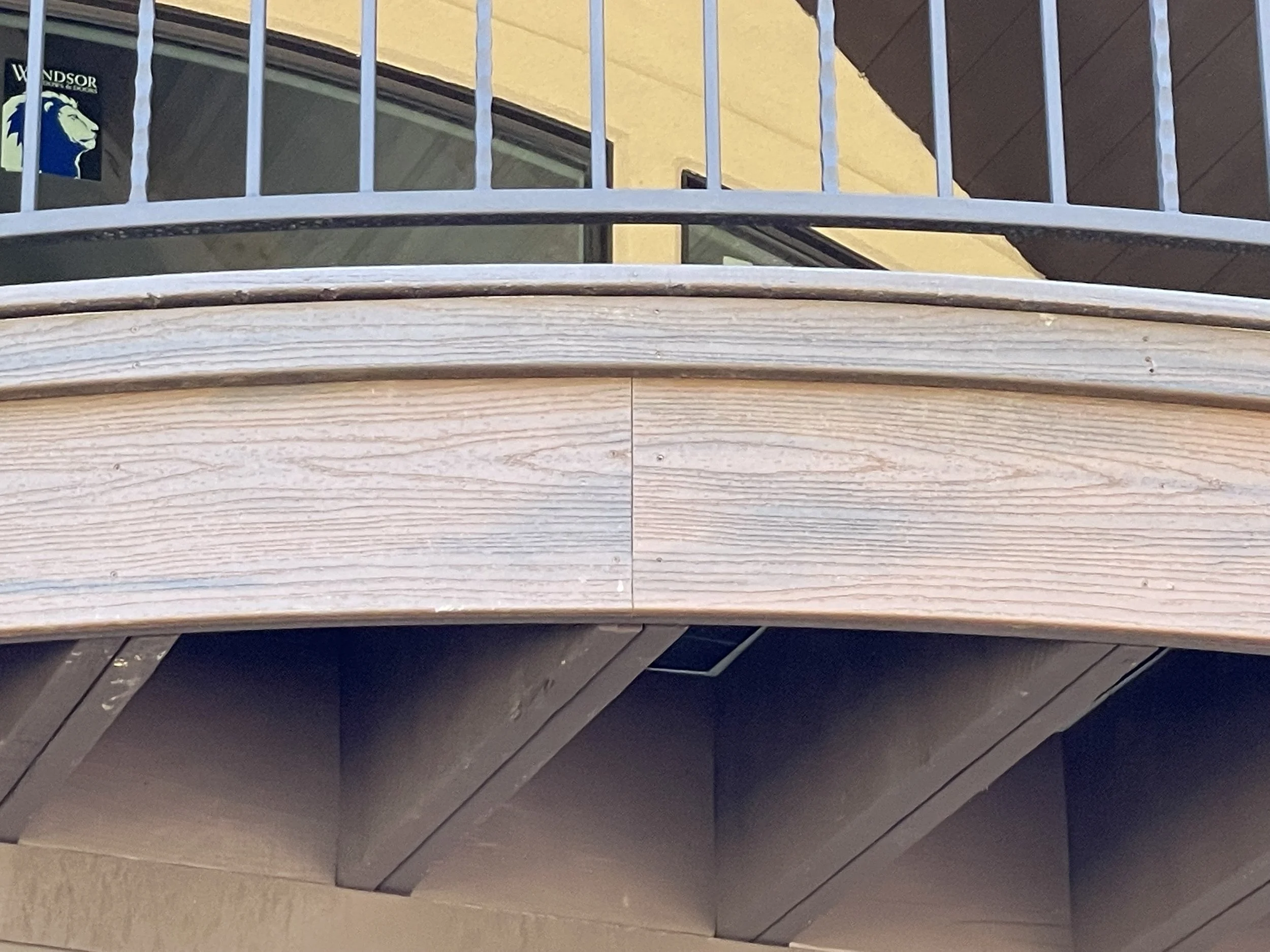 Close-up of a spiral stair railing with black metal stairs and a wooden handrail.