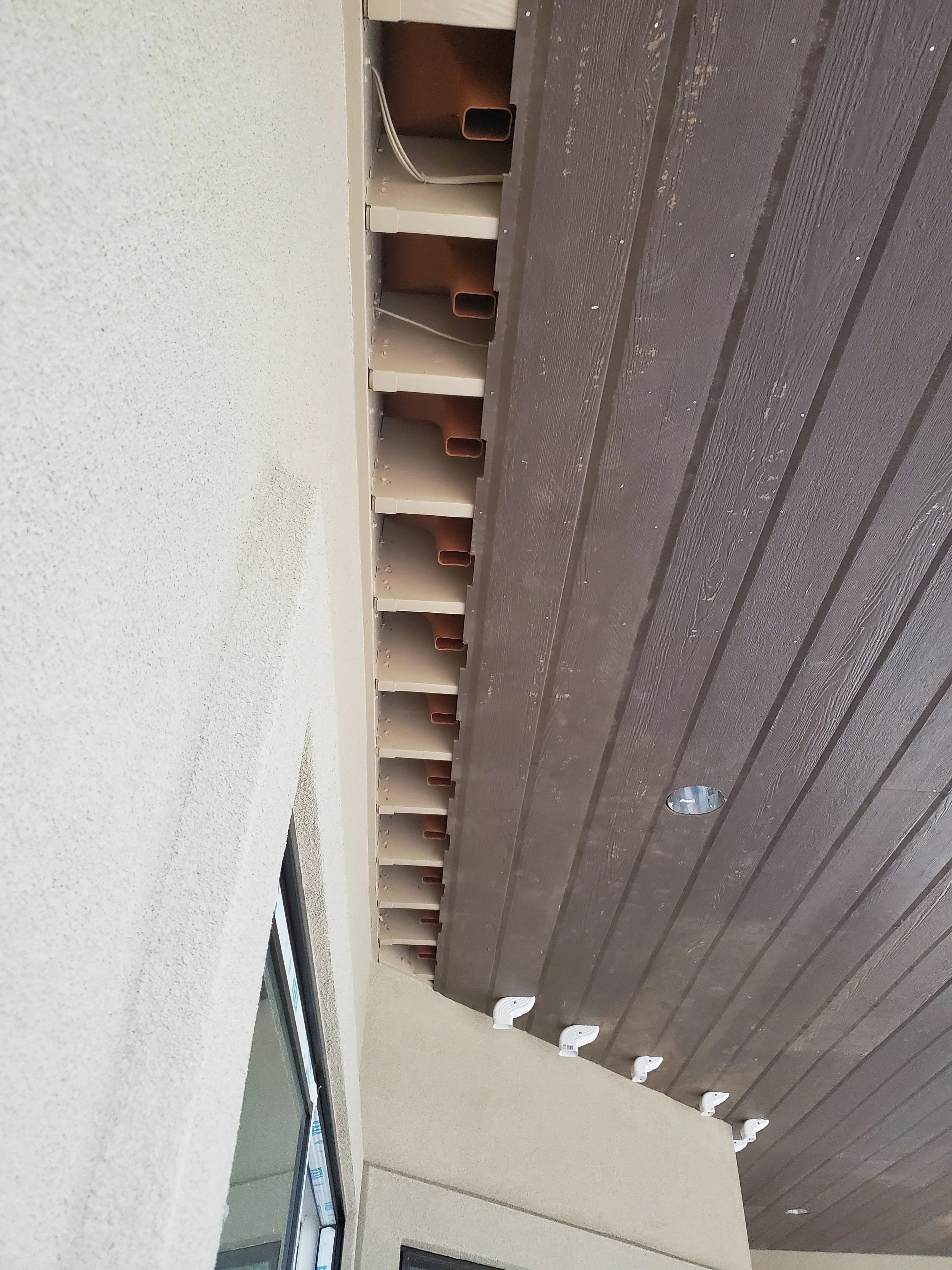 View of a partially constructed or renovated interior wall with exposed drywall and electrical wiring, with a row of brown hooks mounted along the wall and a window with a white frame.