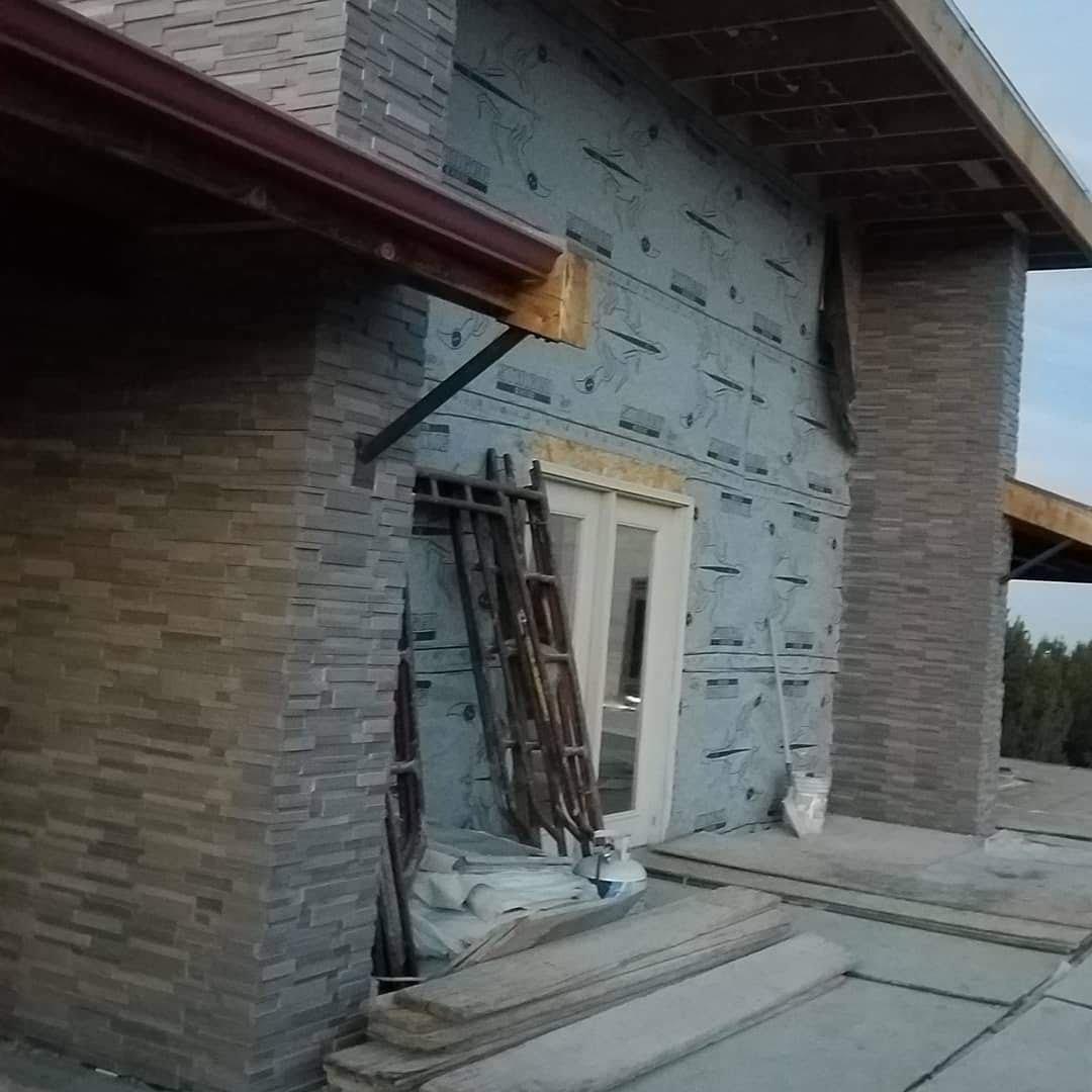 Under construction building exterior with construction materials and ladders resting against wall, partially finished brick wall and siding.