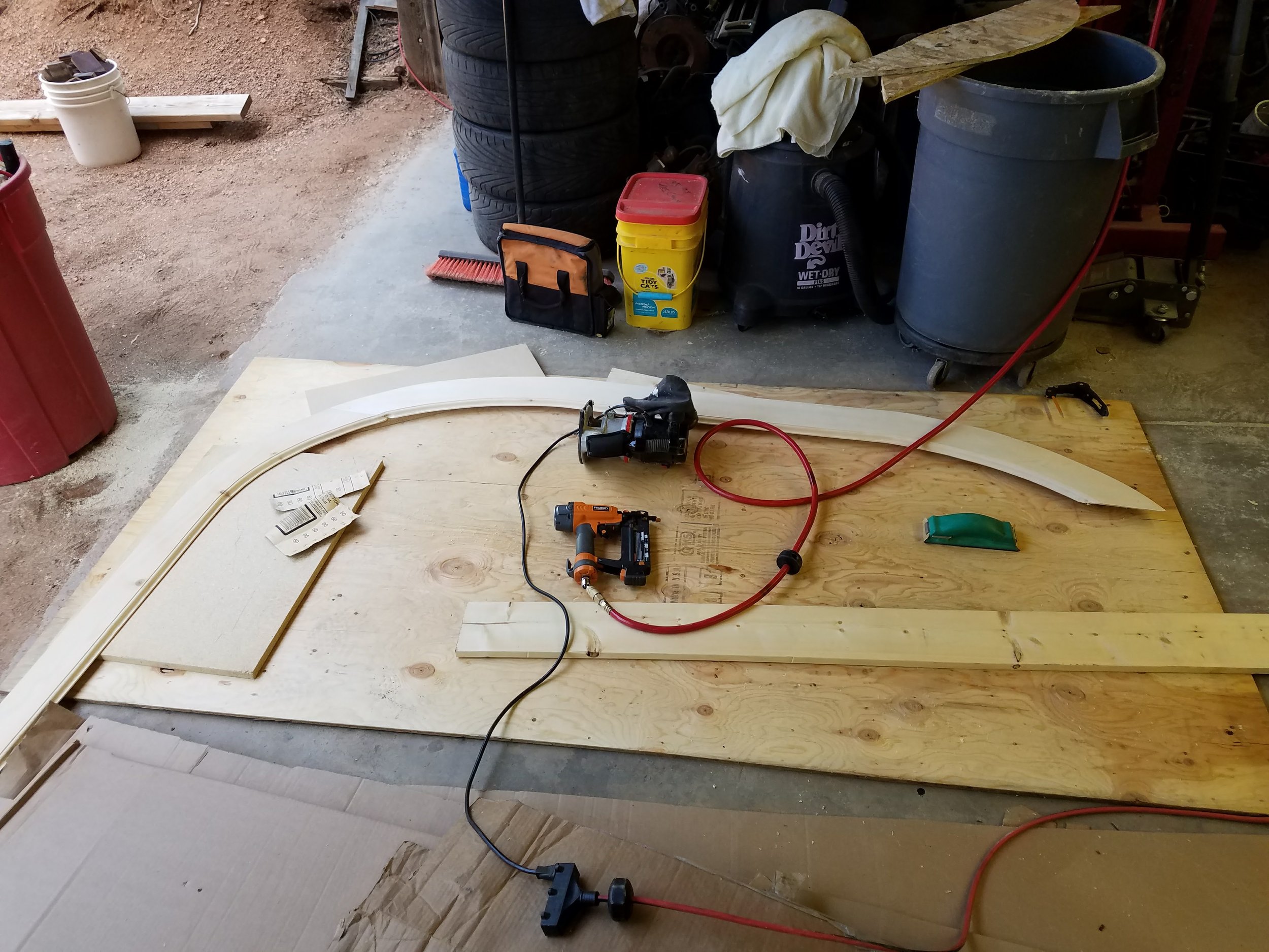 Woodworking workshop with curved wooden pieces, tools, and supplies on a workbench and surrounding area.