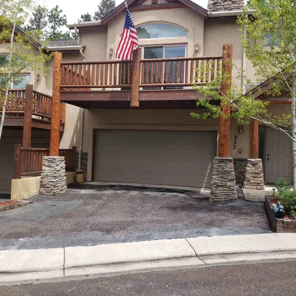 Front view of a house with a stone and wooden deck, an American flag, and a garage door.