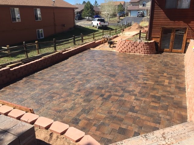 Paved backyard patio with brick walls, a small brick ramp, and a wooden fence, in a suburban neighborhood.