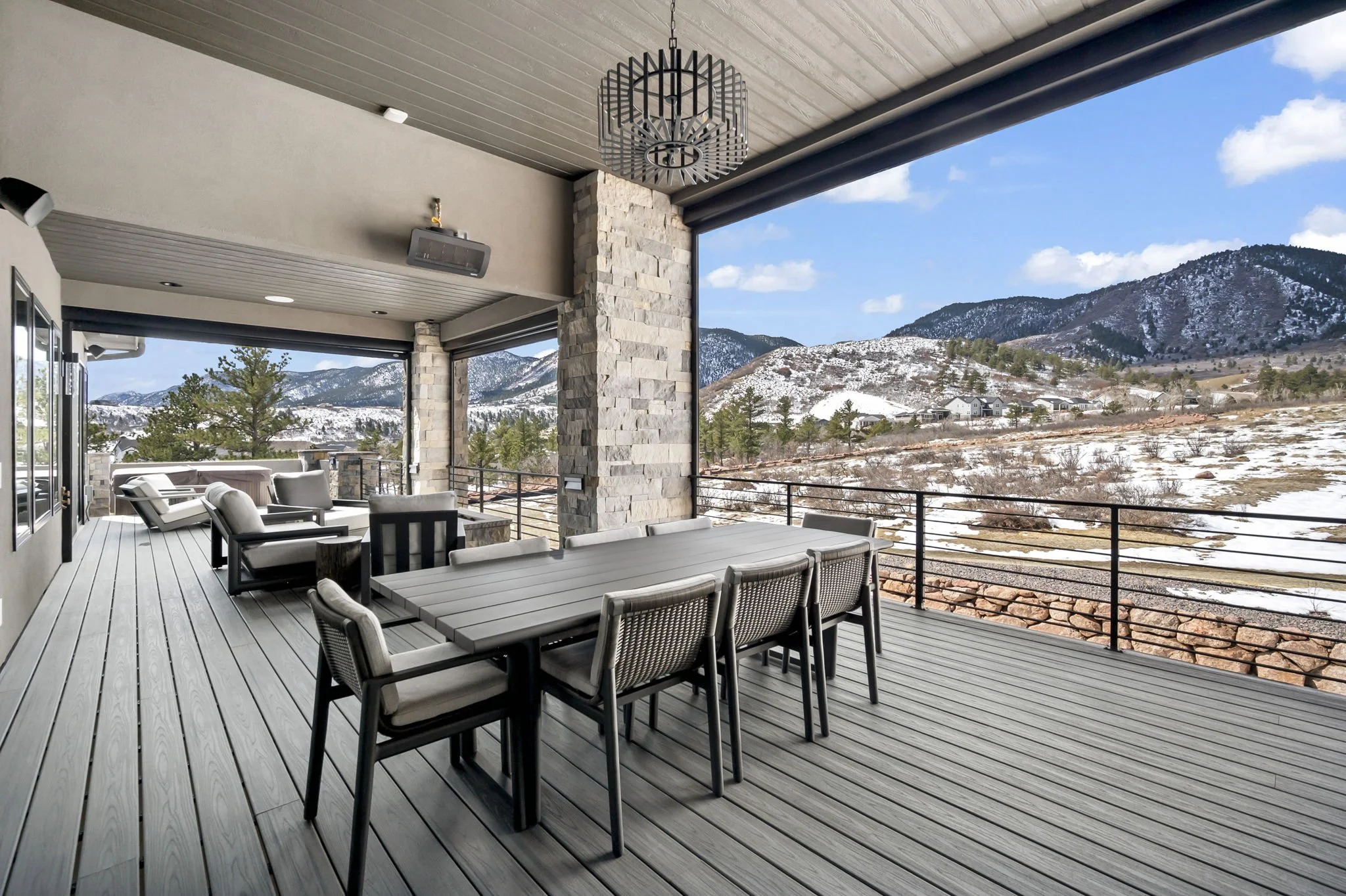 Outdoor patio with dining table and chairs, overlooking a mountainous landscape with snow and trees.