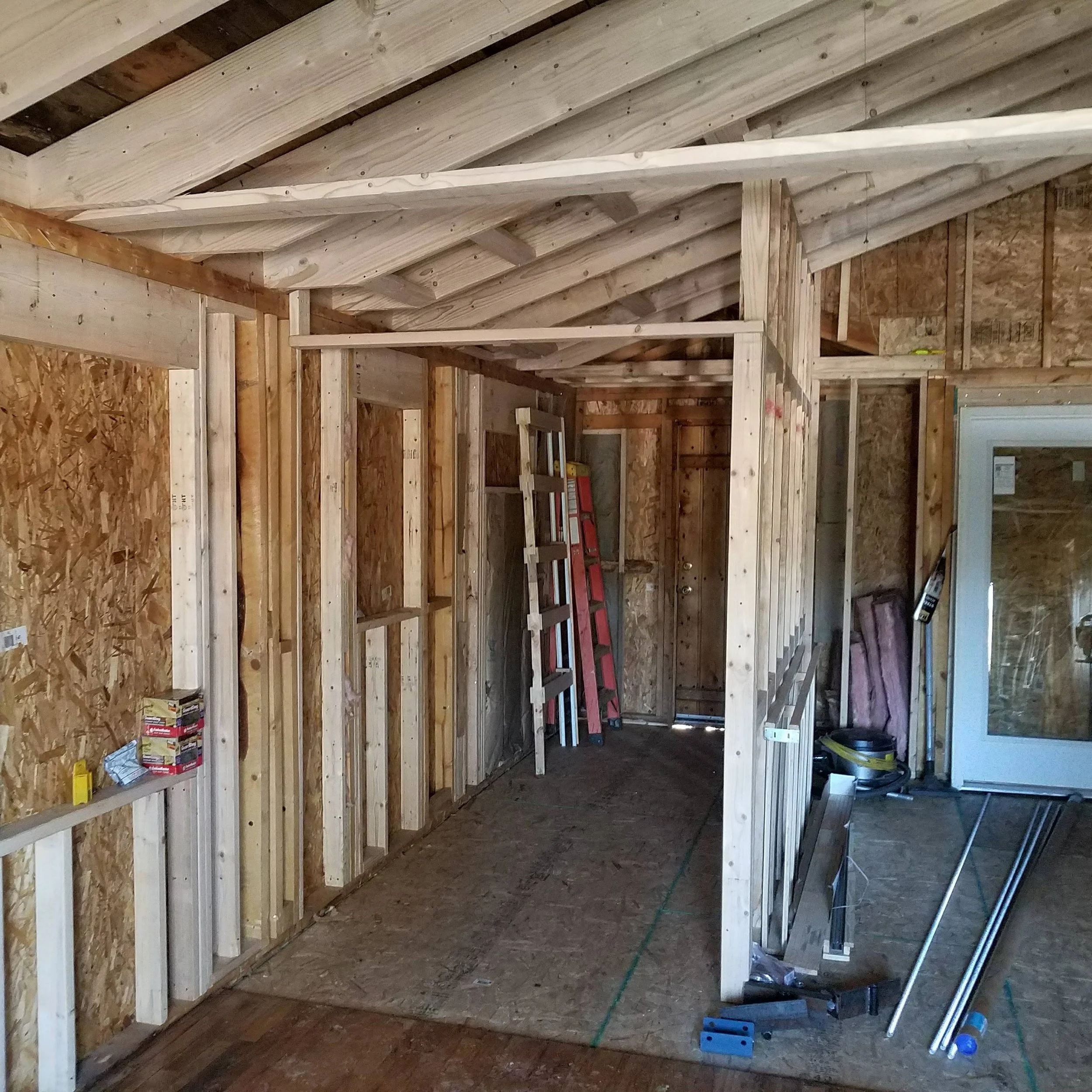 Interior of a building under construction with visible wooden framing, insulation, and construction tools.