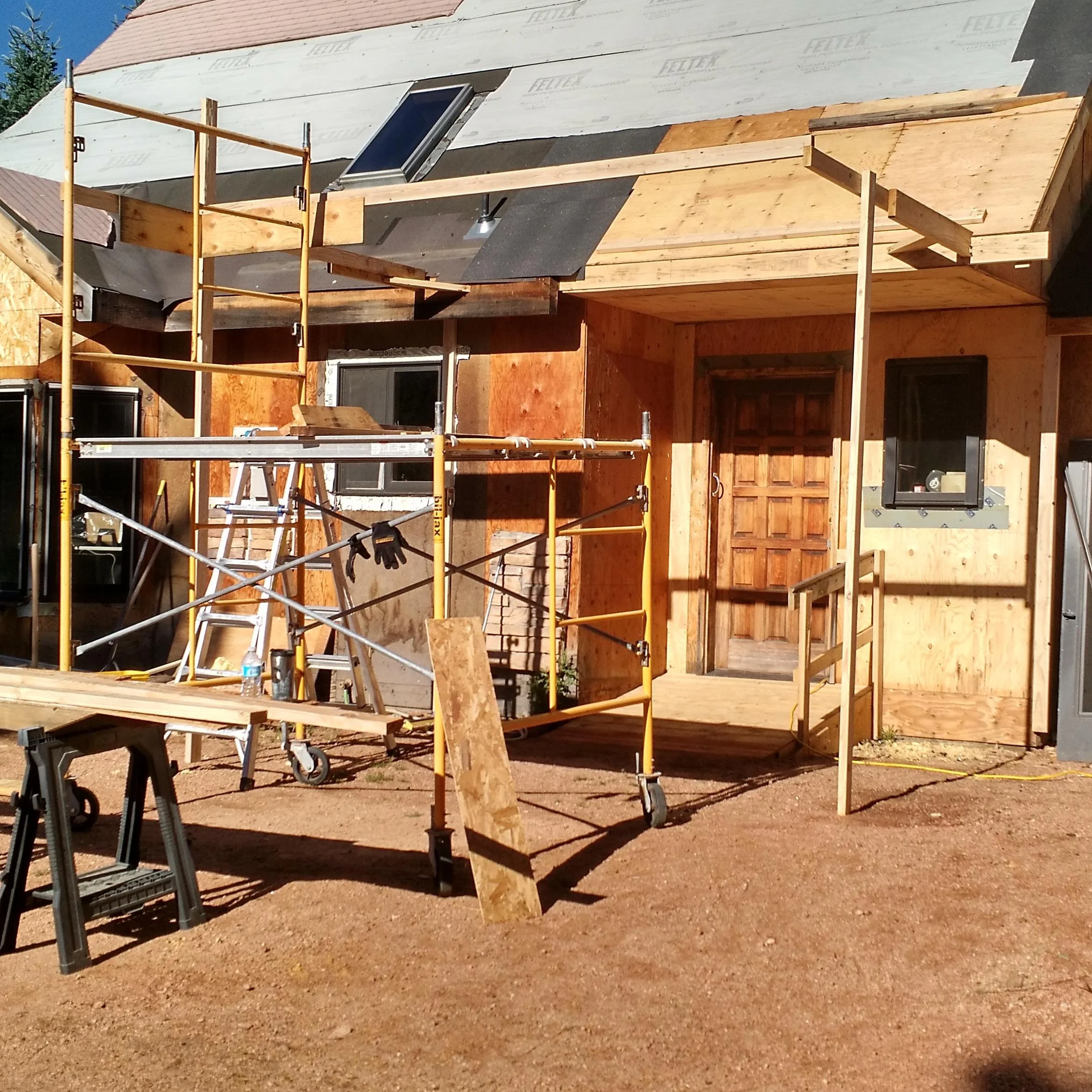 Construction site with wooden framing, scaffolding, and roofing materials in progress on a house.
