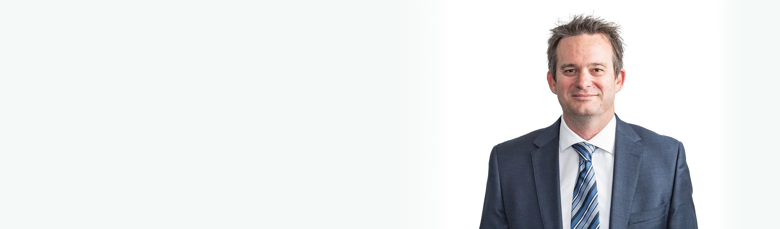 A portrait of a smiling man in a suit and tie standing against a white background.