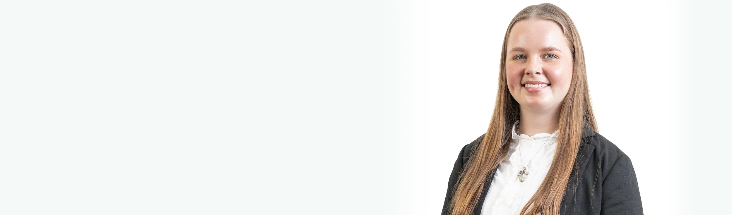 Portrait of a young woman with long red hair, wearing a white blouse and black blazer, smiling against a plain white background.