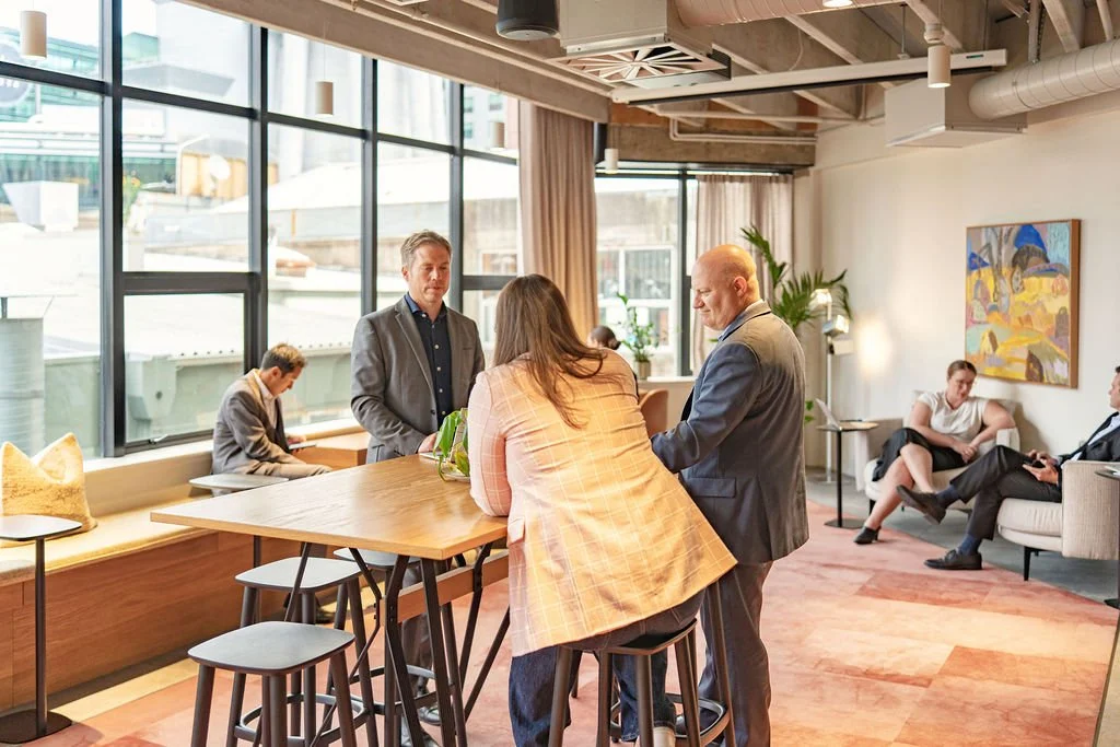 People talking in a modern office lounge with large window and art on the wall.
