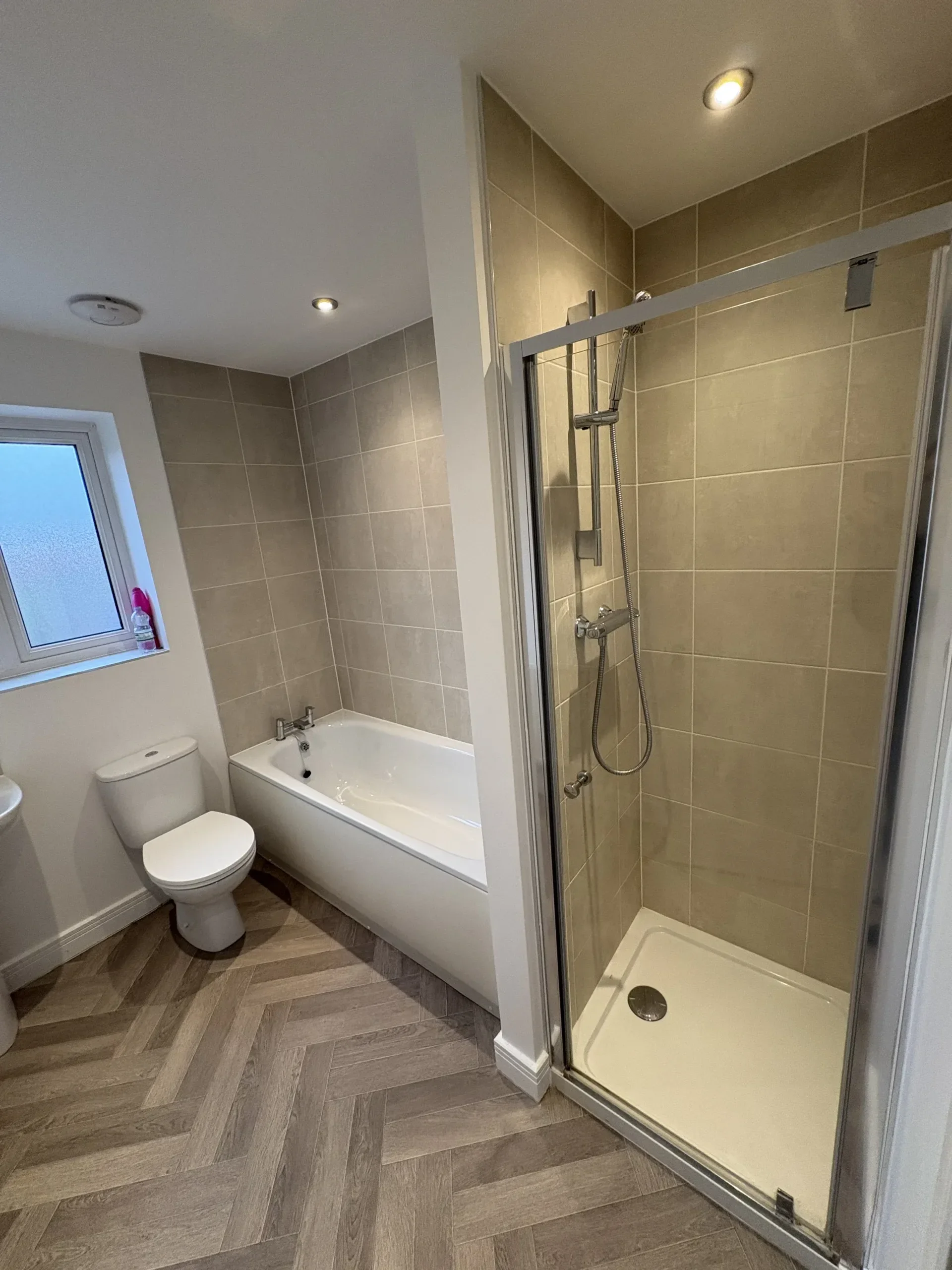 Bathroom with a window, a white toilet, a bathtub, and a shower enclosure with beige tile walls.