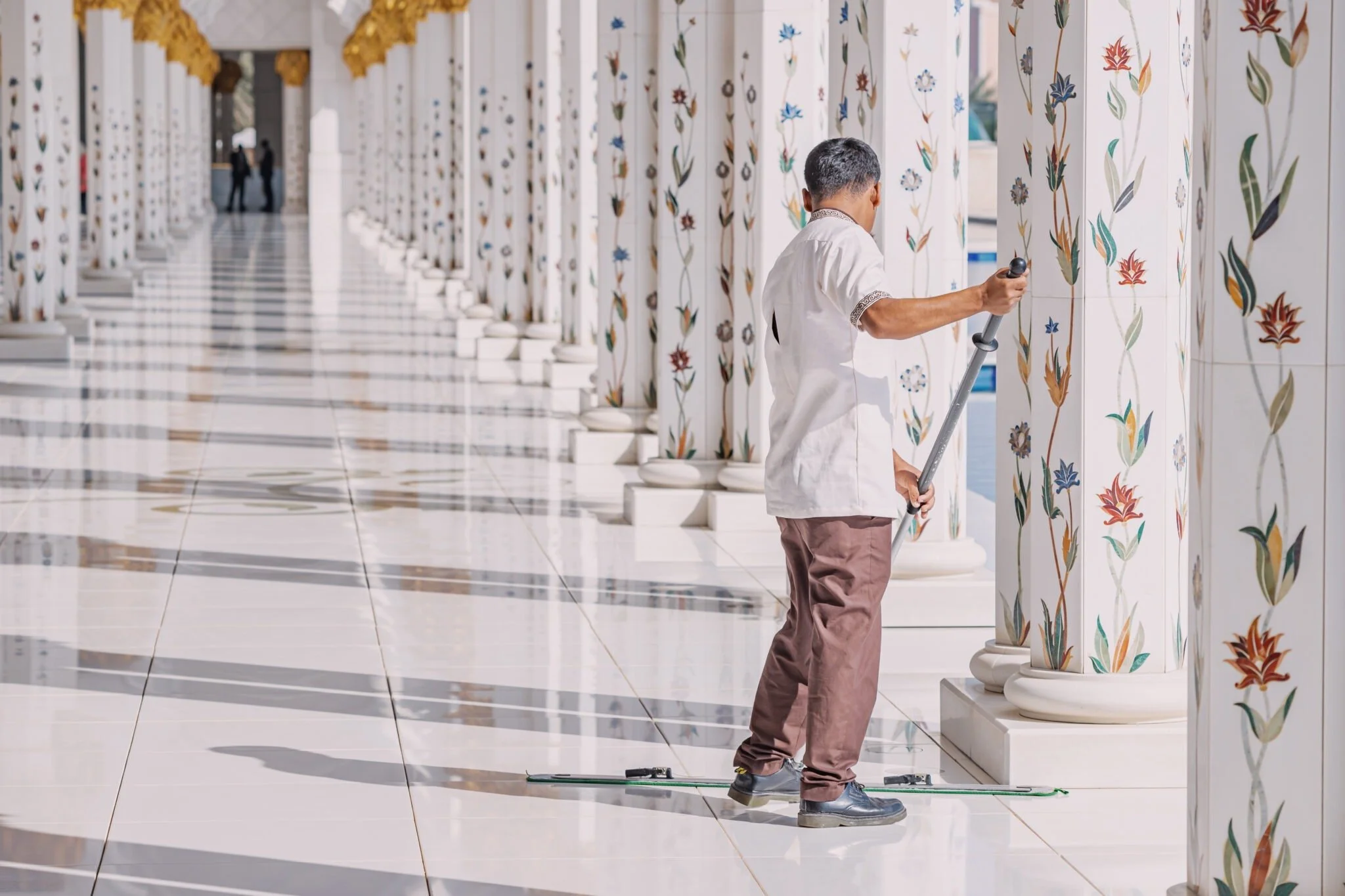 A worker polishing marble columns with floral designs at a mosque.