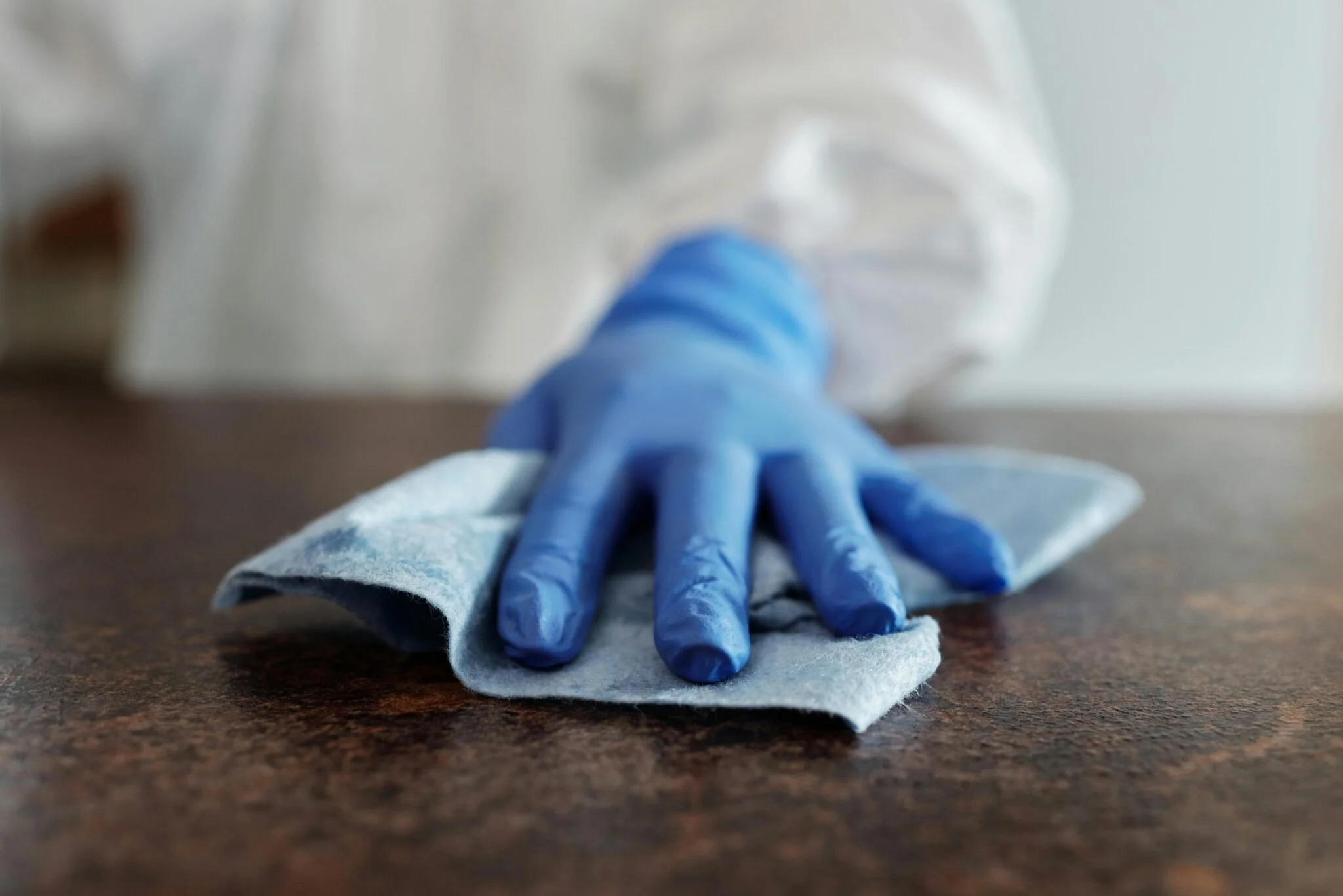 Person in protective gear cleaning a wooden surface with a cloth.