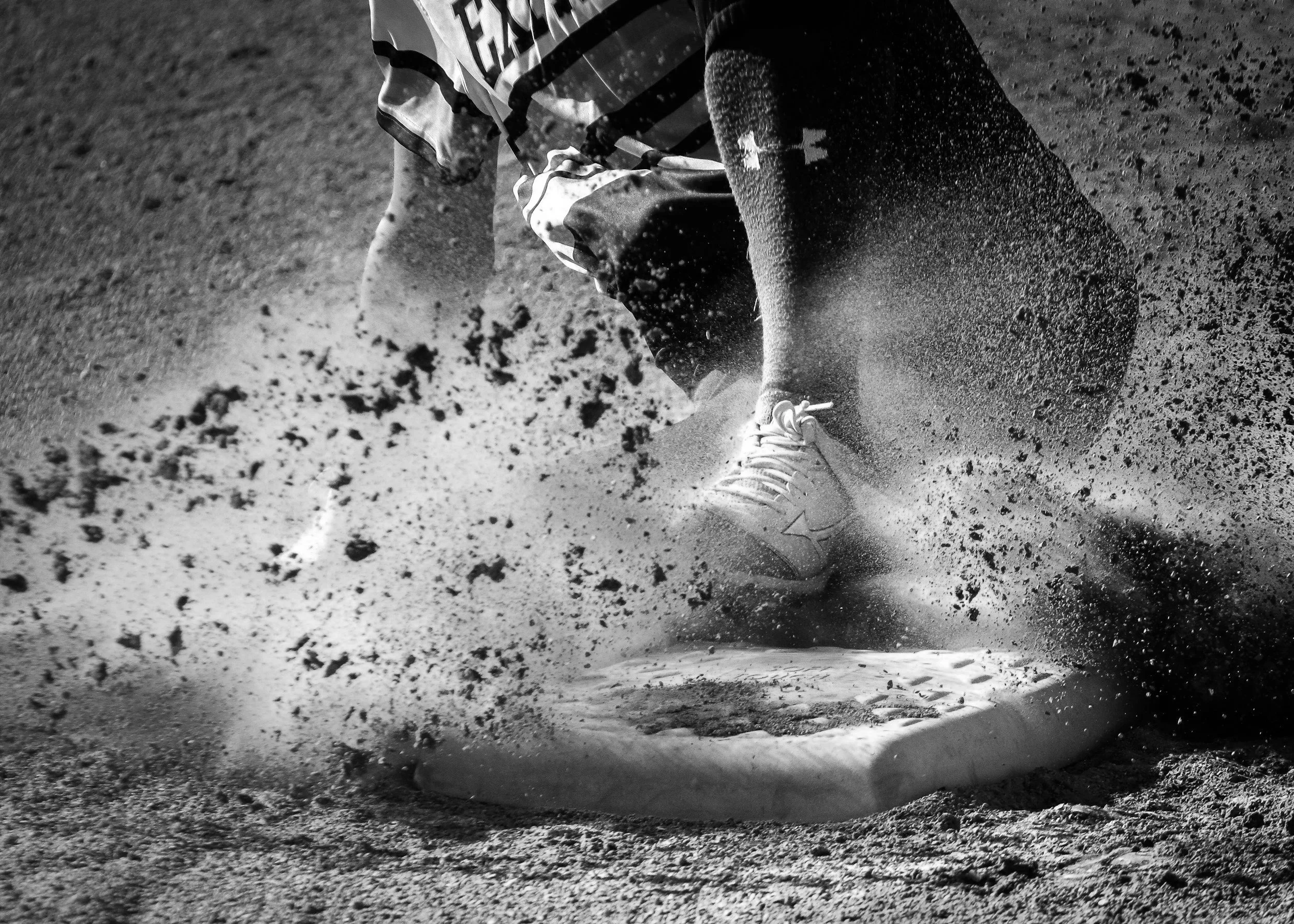 A person wearing athletic shoes and sportswear lying on the ground, kicking up dust and dirt on a gravel or dirt surface.