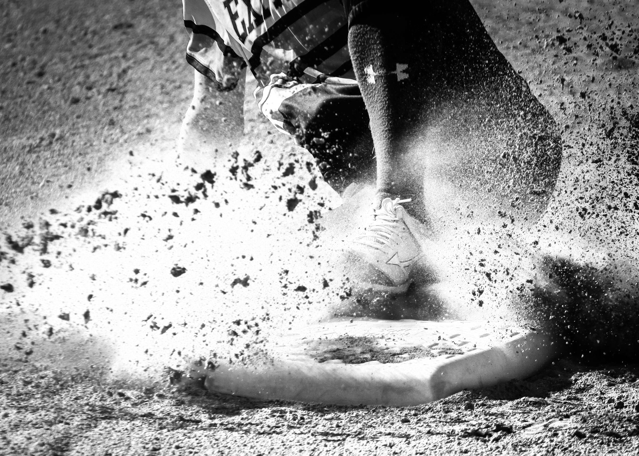 A person in athletic clothing and sneakers running on a dirt or gravel trail, kicking up dust and small rocks.