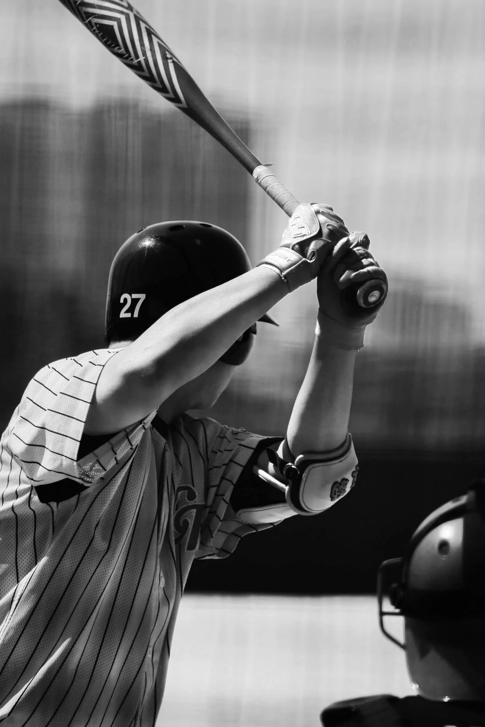 A baseball player wearing a striped jersey and batting helmet, swinging a bat during a game or practice.