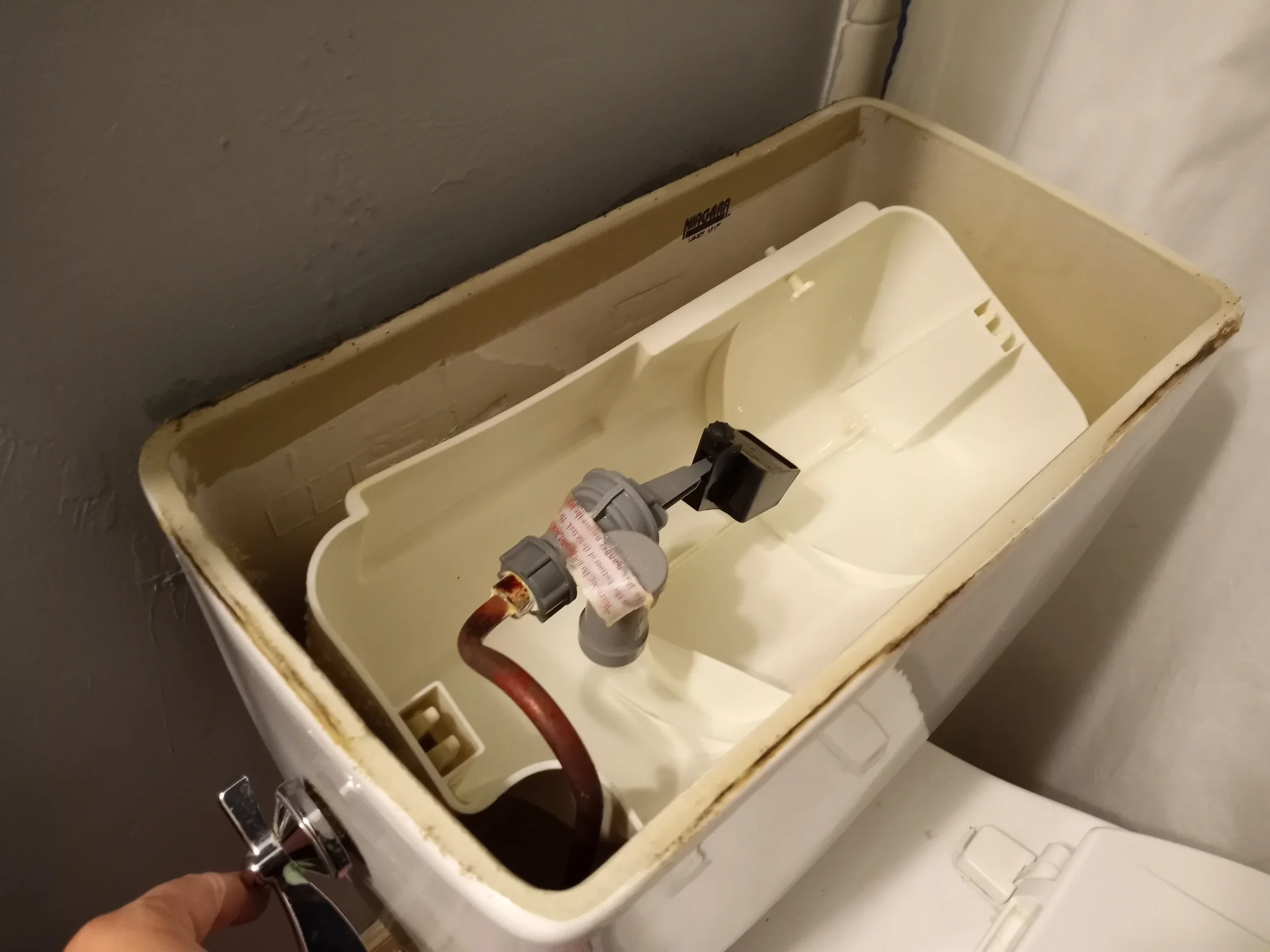 Open toilet tank with internal components and a person's hand holding a toilet handle.