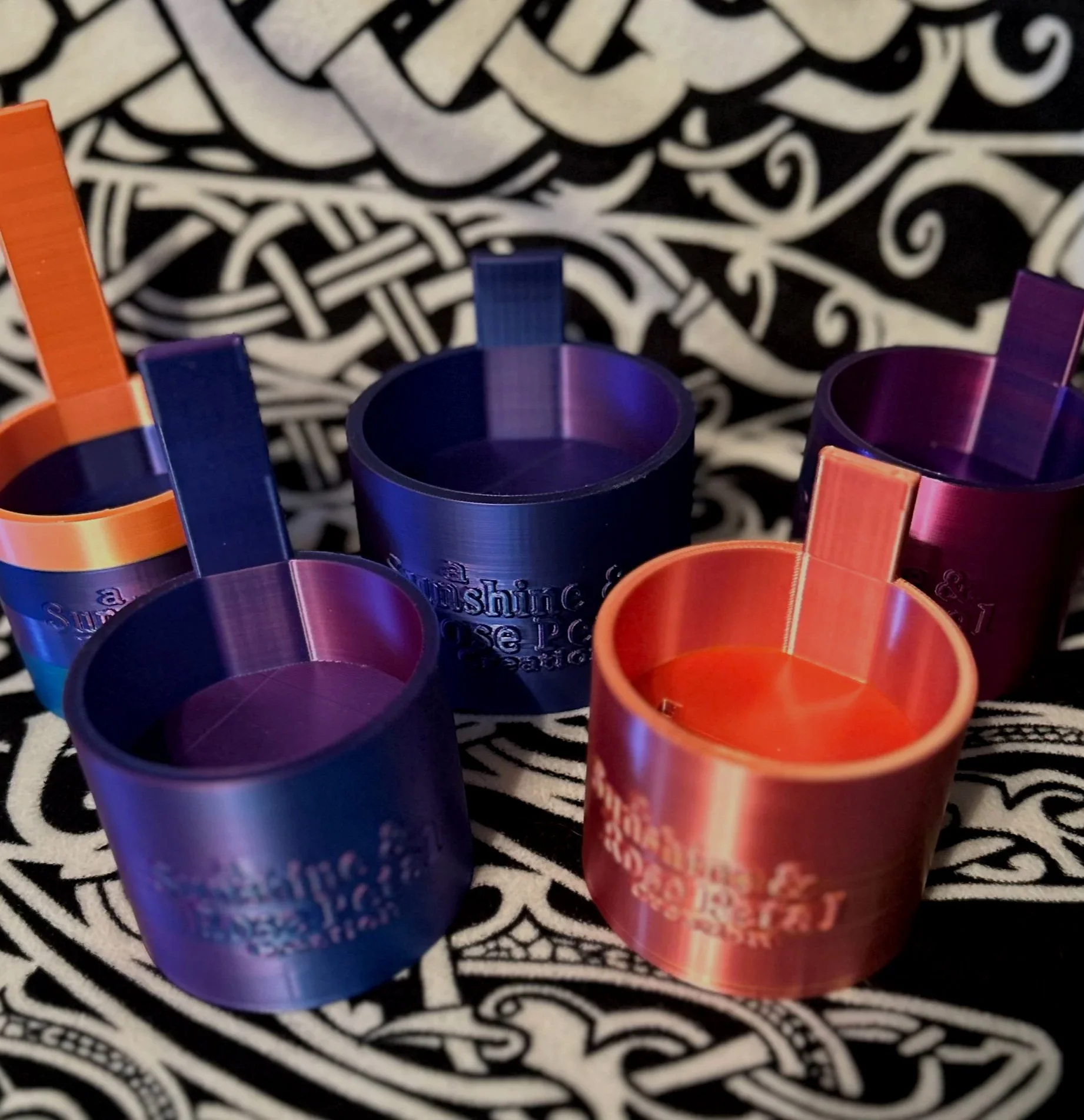 Several colorful plastic shot glasses with straws on a decorative black and white patterned surface.