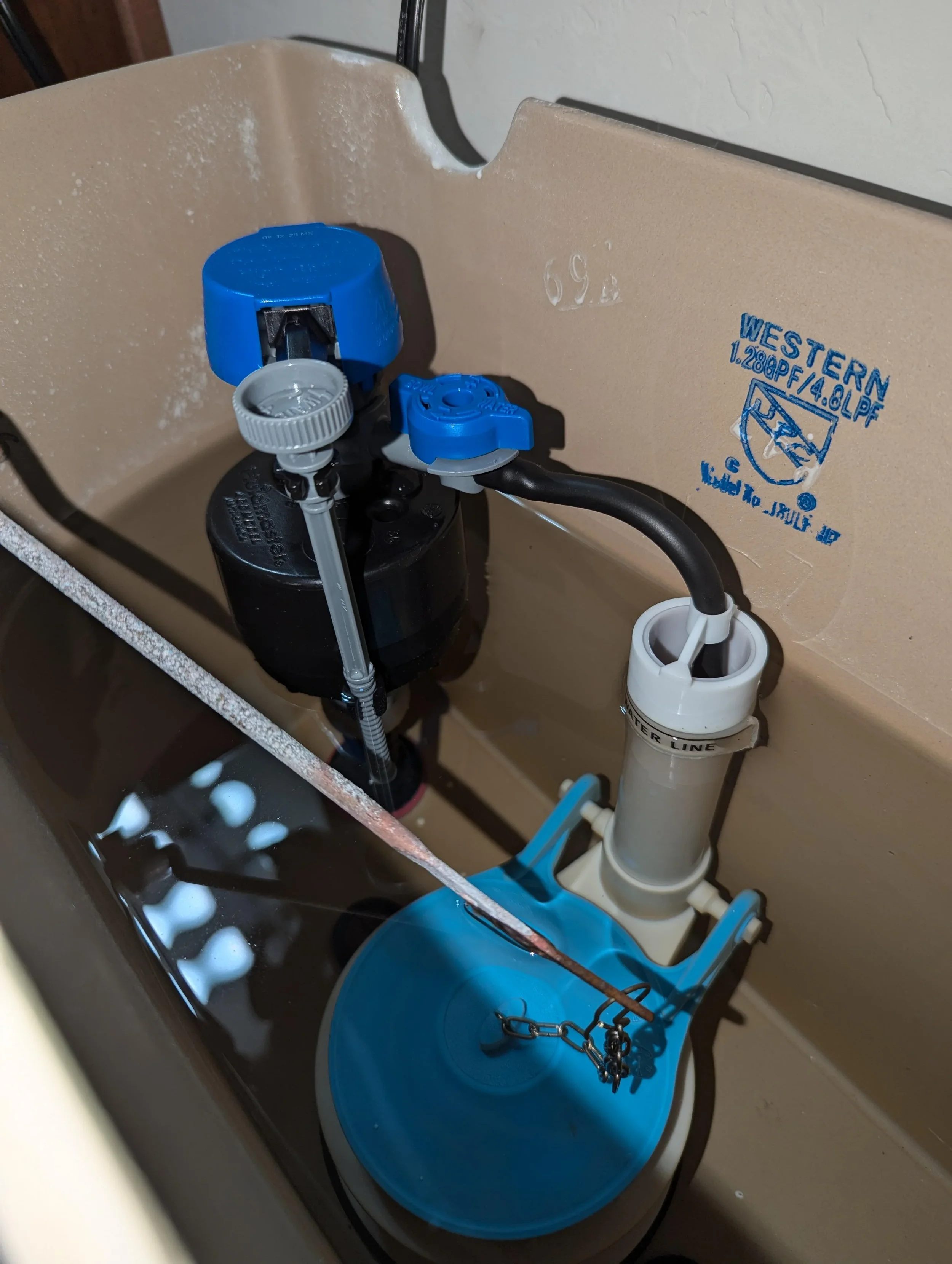 Inside a toilet tank, showing a fill valve, float, and flapper system with water.