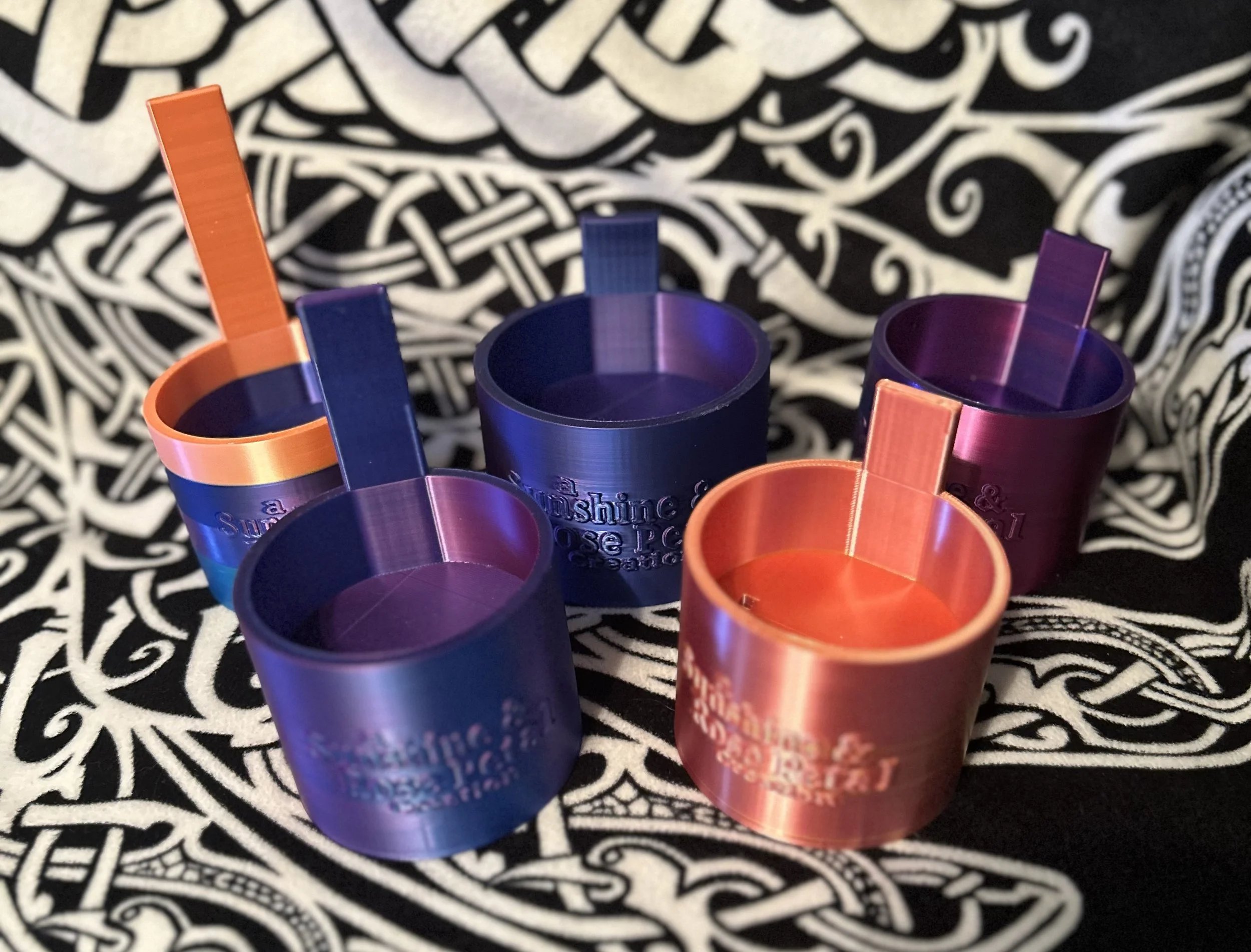 Five metallic spinning tops in blue, purple, and orange colors arranged on a black and white patterned cloth.