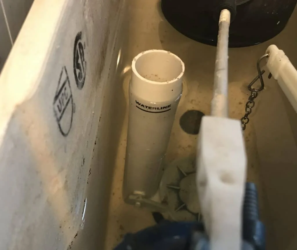 Close-up of plumbing inside a toilet tank showing a water level tube, fill valve, and chain.