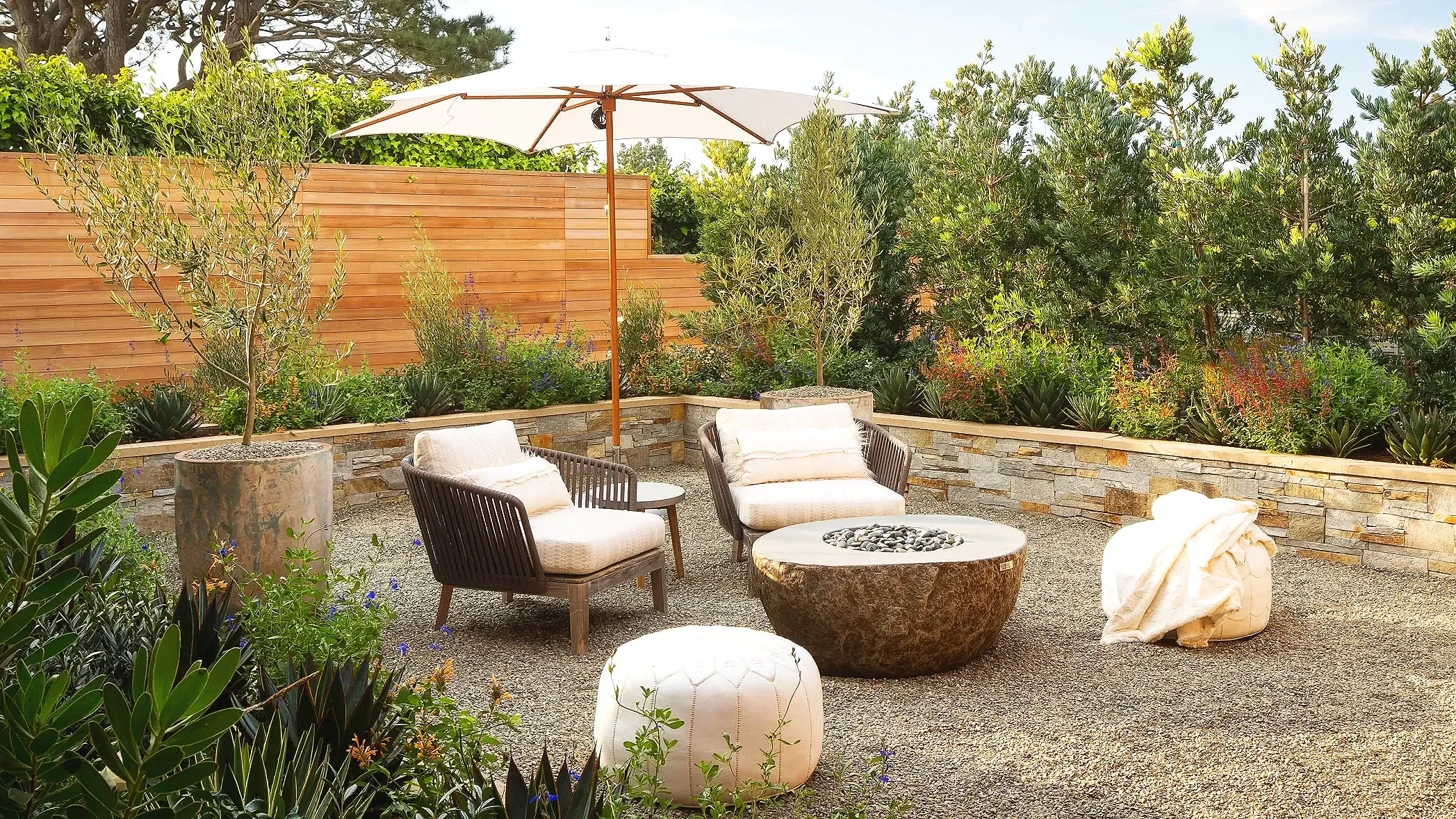 Relaxing outdoor patio area with chairs, a fire pit, an umbrella, and greenery.
