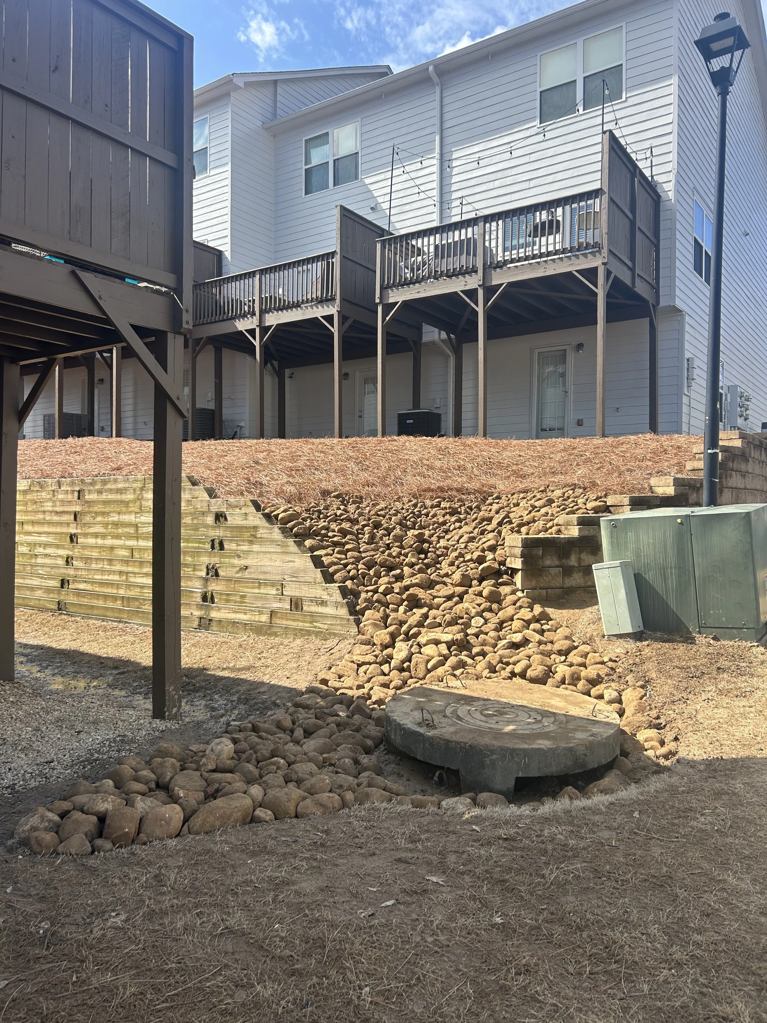 Backyard scene with a wooden deck, stone pathway, and white townhouses with balconies.