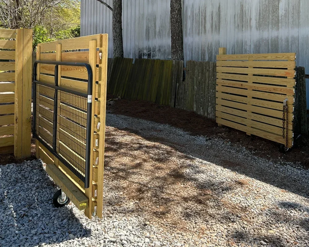 Exterior yard scene with two wooden gates, one attached to a fence, and the other leaning against a wall, with a gravel pathway and a weathered wood fence in the background.
