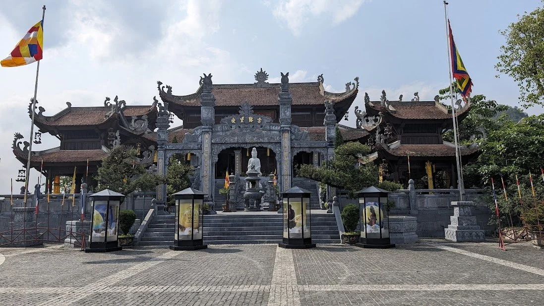 Traditional Asian temple with ornate rooftops and a central statue, surrounded by flags and lanterns.