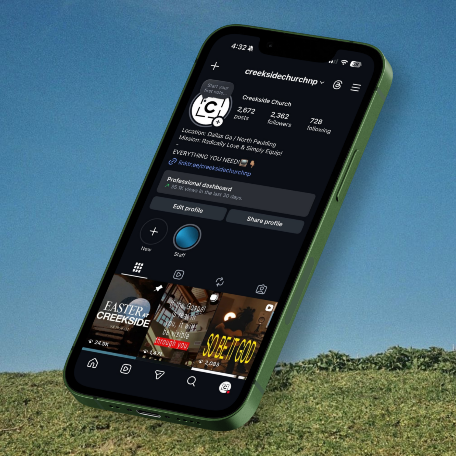 A smartphone in a green case displaying a social media profile for Creekside Church, showing posts about Easter and religious messages, against a grassy outdoor background with a clear blue sky.