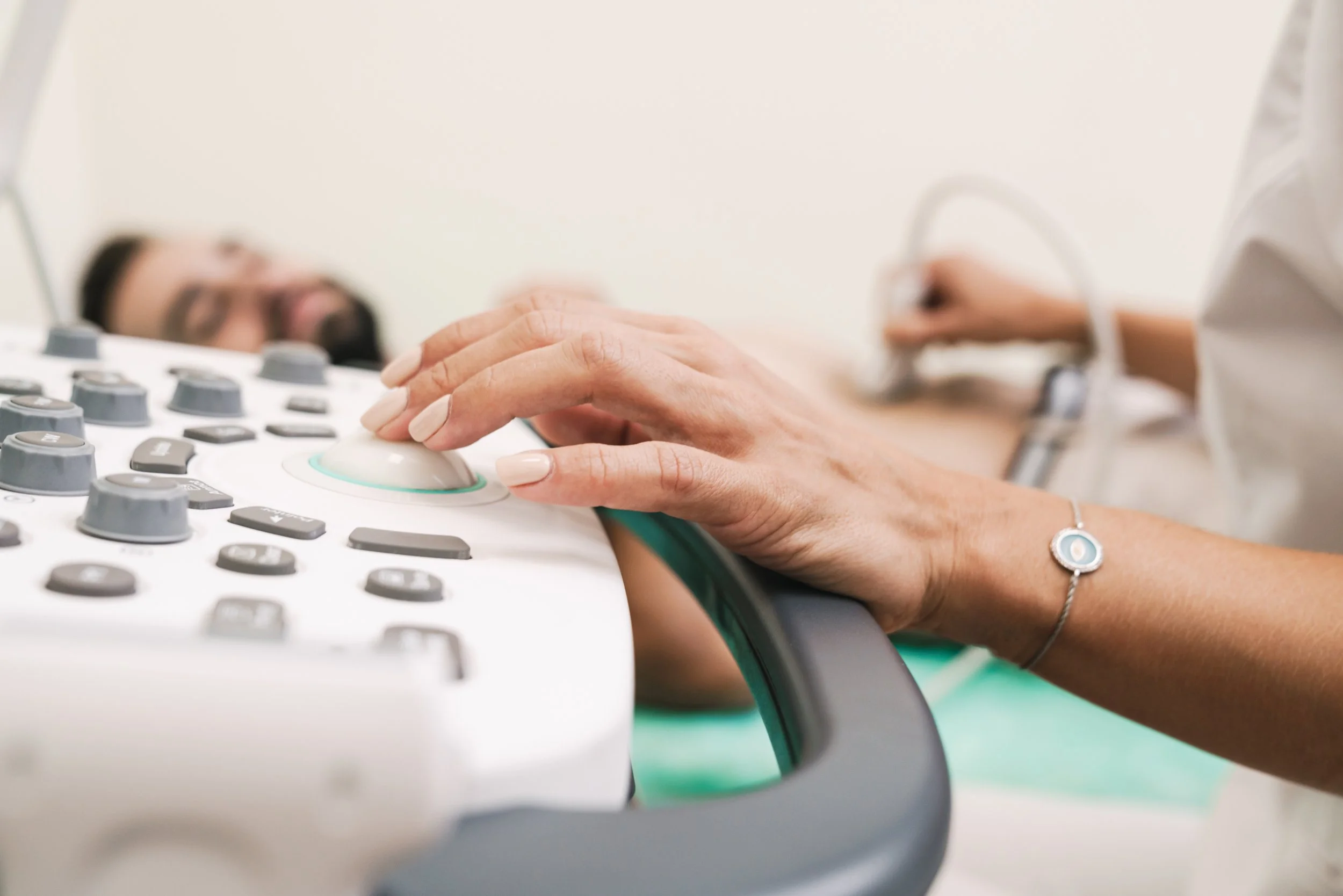 Close-up of a person's hand using a medical device with numerous buttons, with a blurred face of a person in the background.