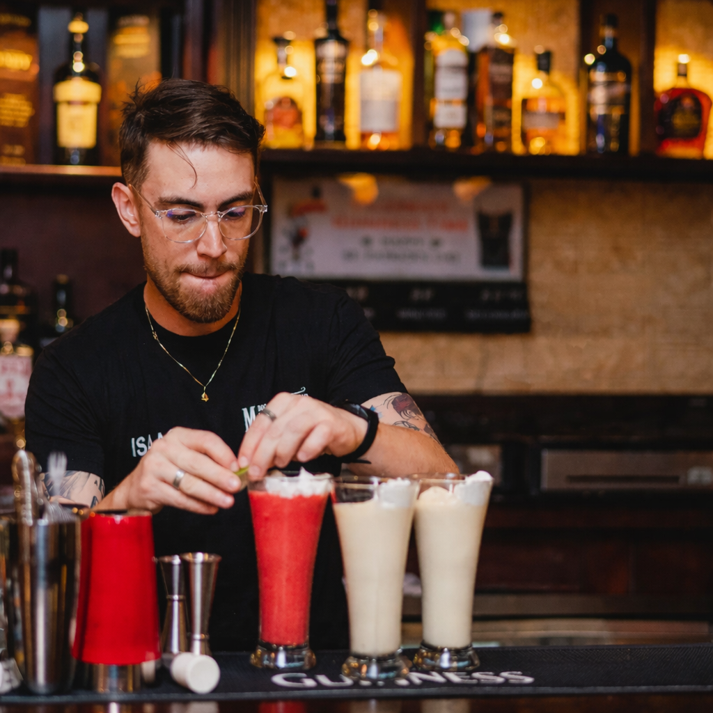 Bartender preparing garnishes for cocktails in a bar with bottles on the shelves in the background.
