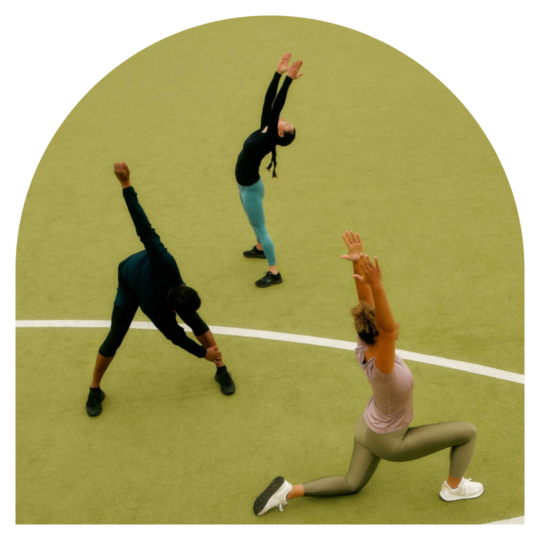 Three people exercising in a gym, performing stretching and yoga poses on green flooring.