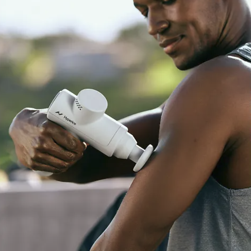 A man applying a Hyperice recovery massage gun to his arm