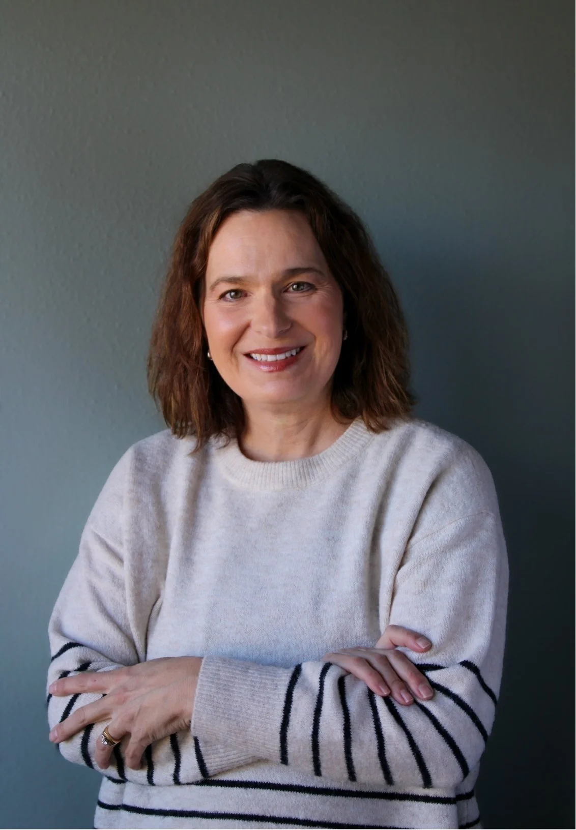 Dr. Renee Woodall, therapist in Fort Collins, CO, smiling, wearing a cream-colored sweater with black stripes on the sleeves, against a dark gray background.