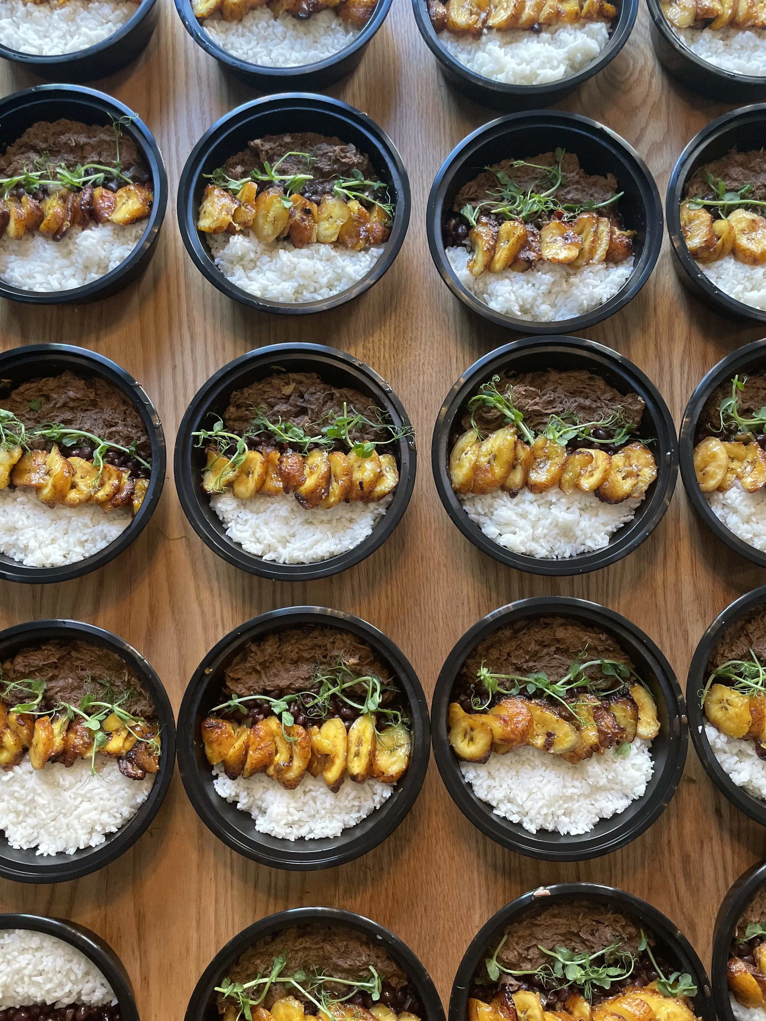 Portioned meals of rice, plantains, and Venezuelan carnitas